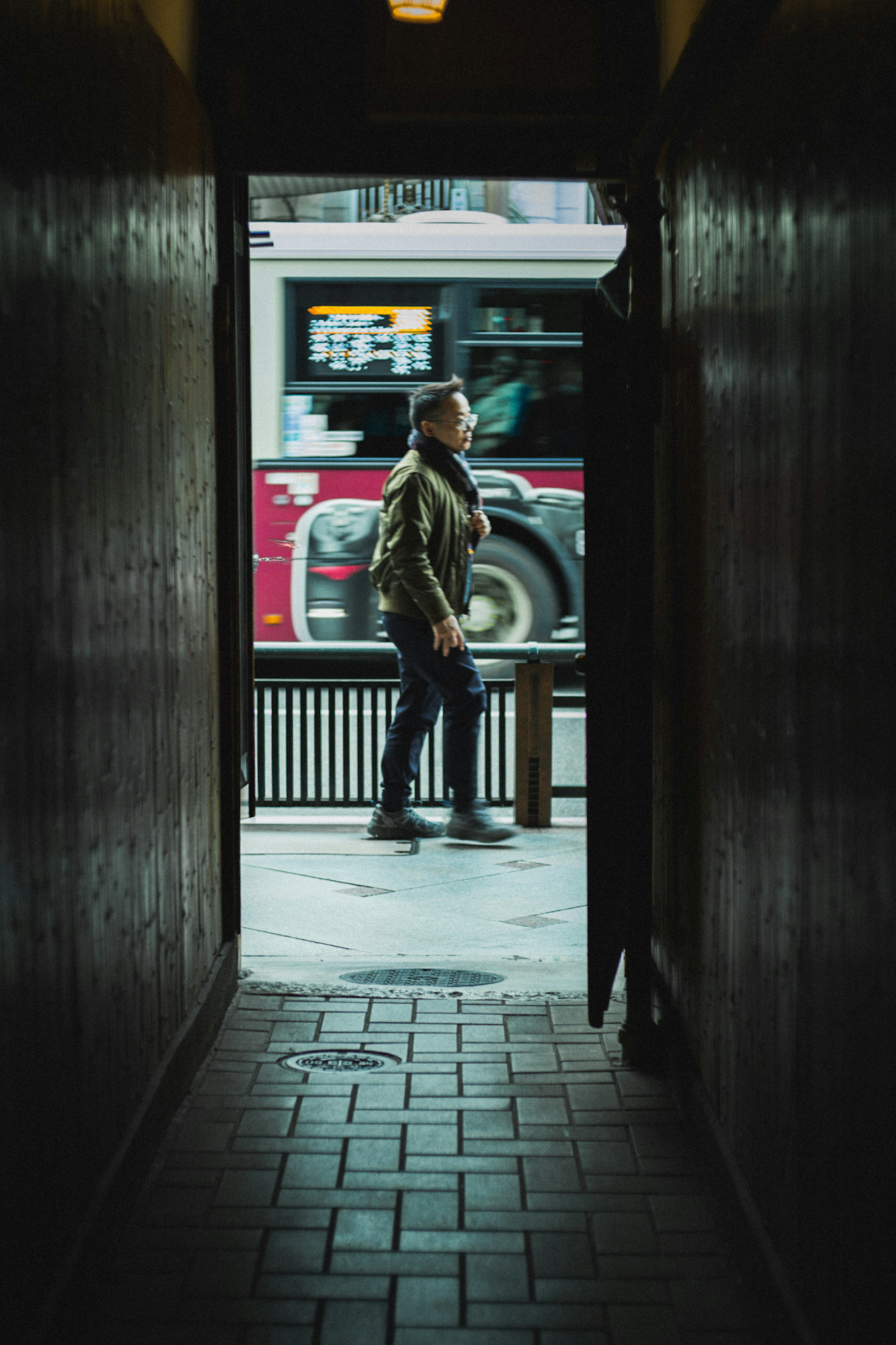 A person walking outside visible through a narrow corridor with a bus in the background