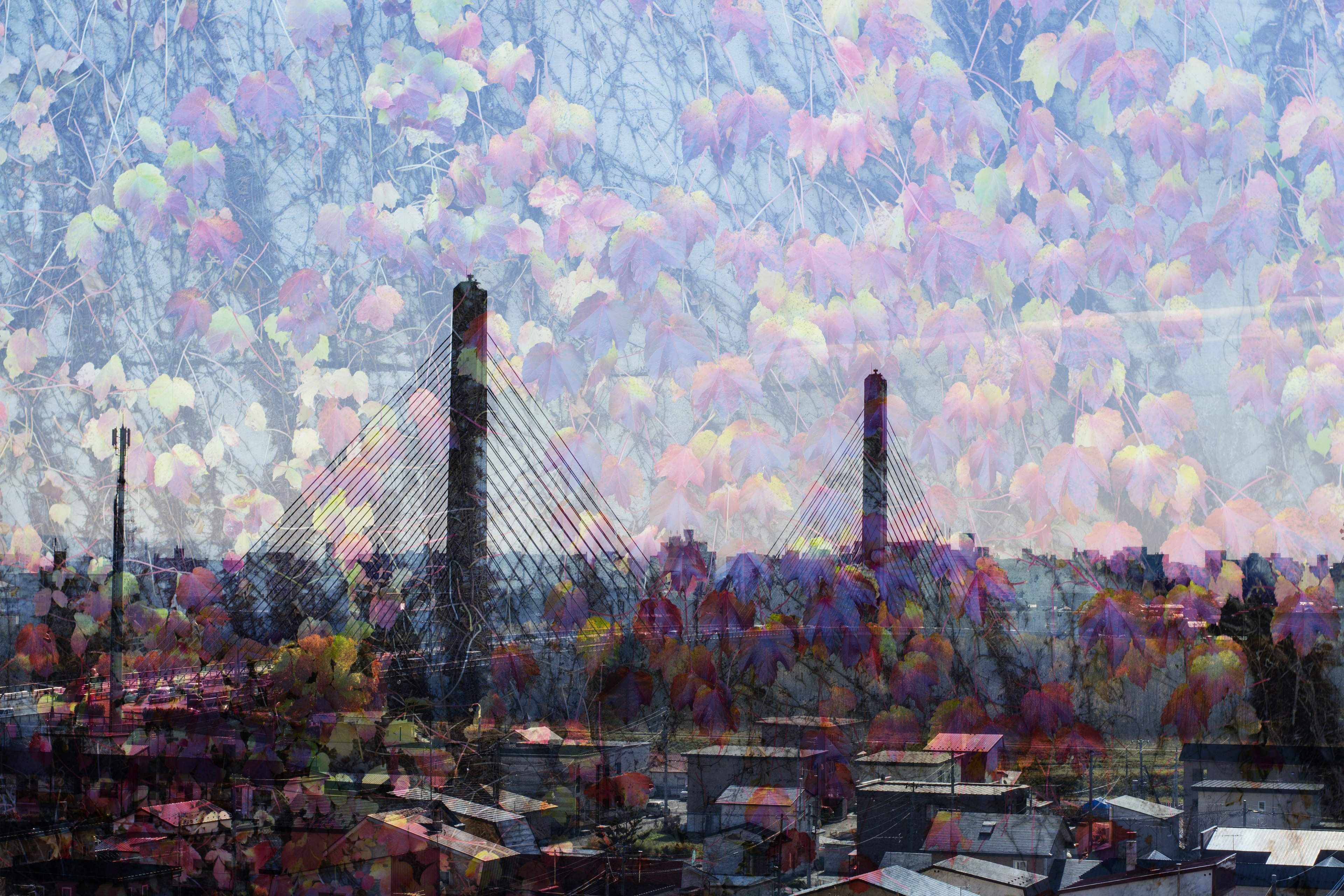 色とりどりの雲が広がる空の下に高層ビルと煙突が見える都市の風景