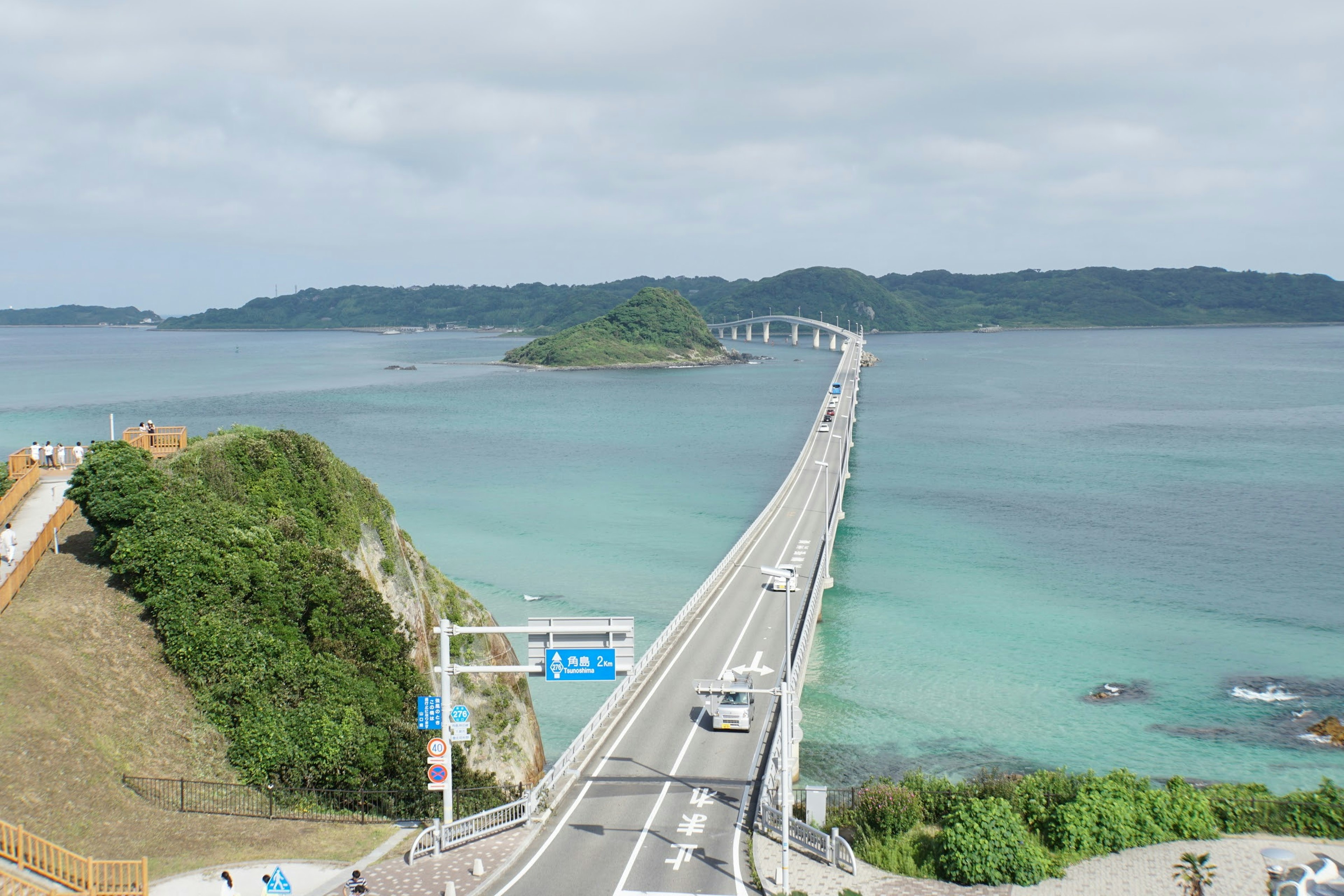 Pemandangan jembatan di atas laut biru dengan bukit hijau dan pulau kecil