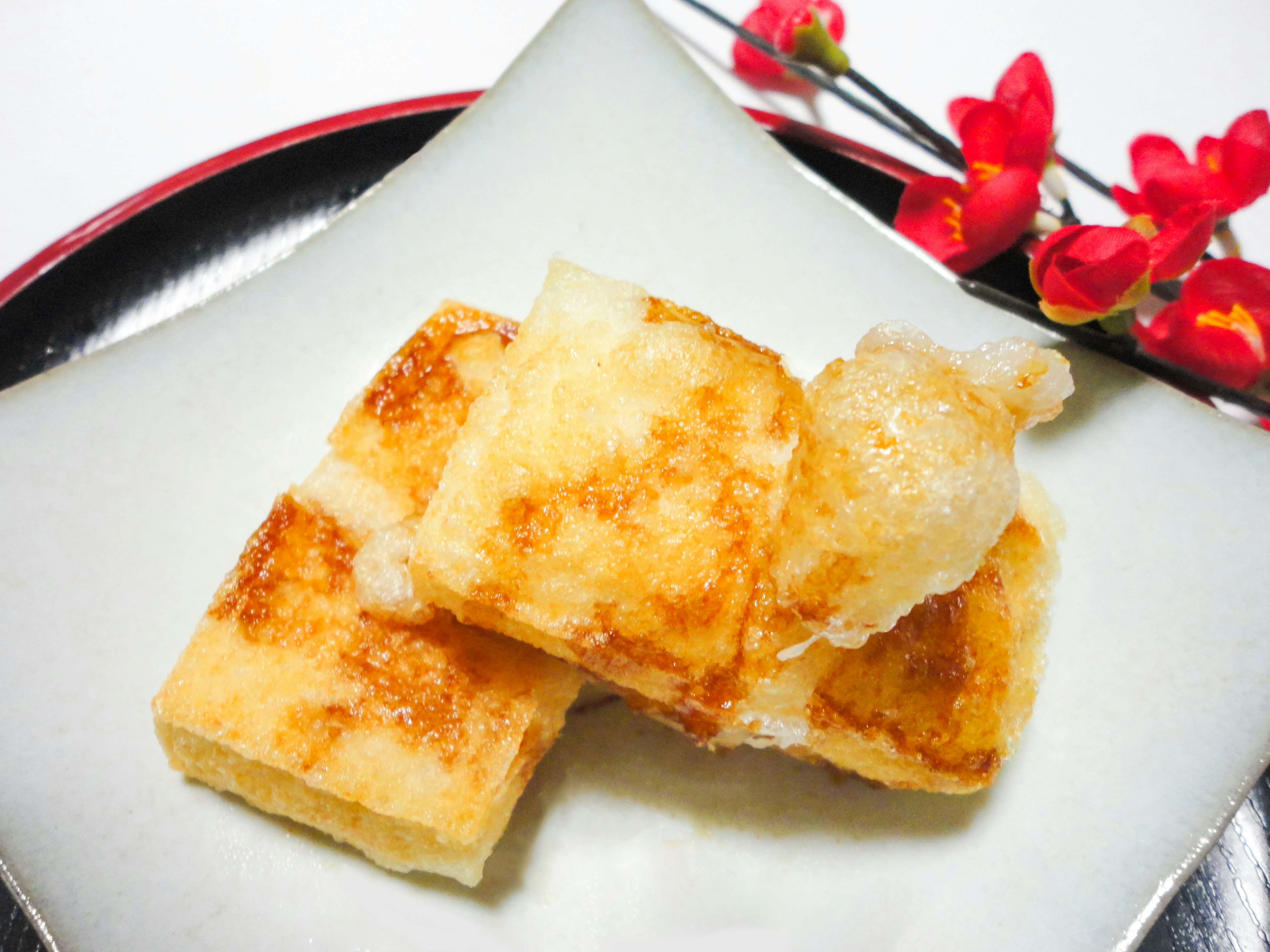 Un plato de pasteles de arroz fritos dorados dispuestos en un plato blanco con flores rojas decorativas