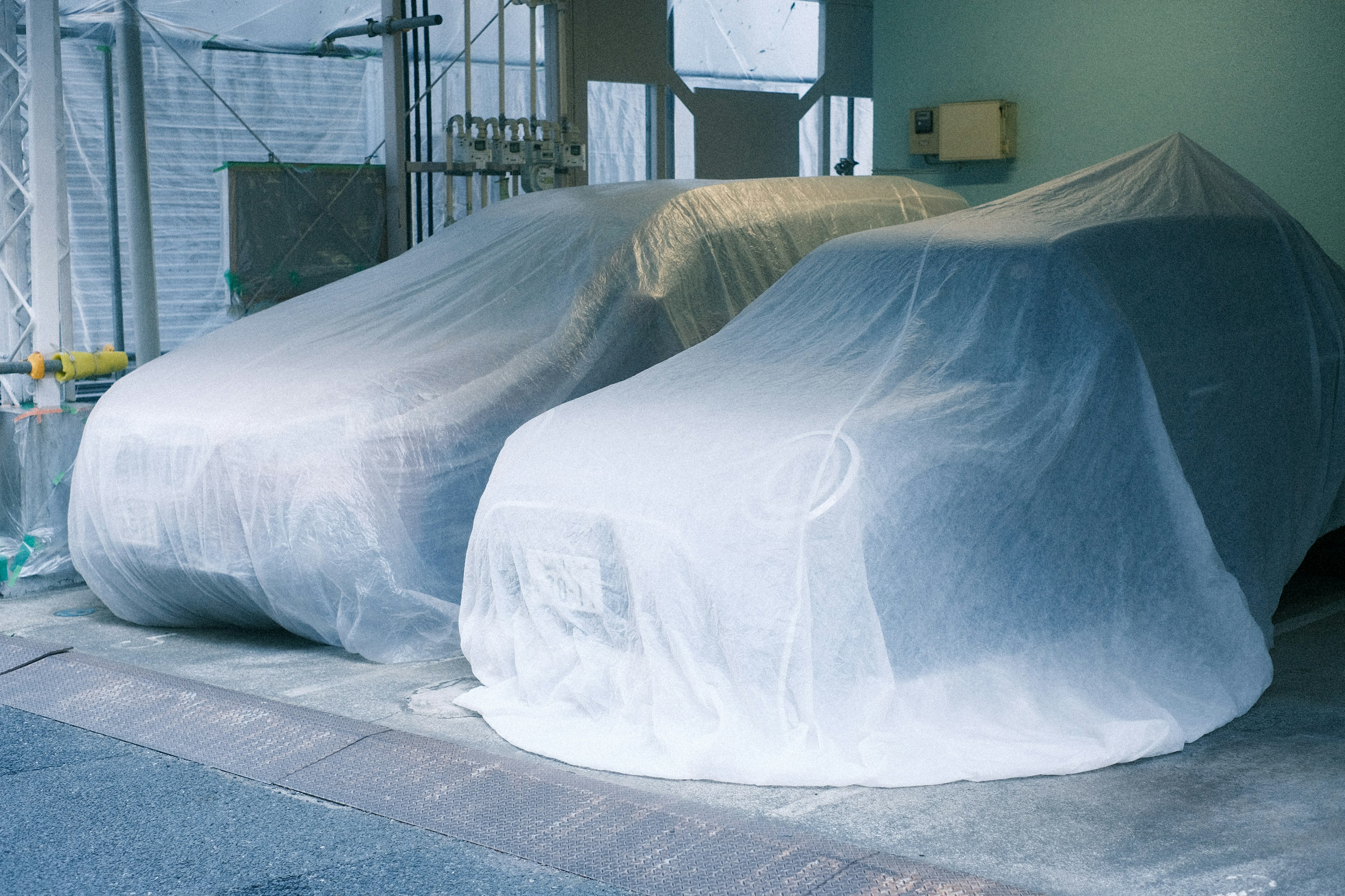 Zwei Autos, die mit weißen Abdeckungen in einer Garage bedeckt sind