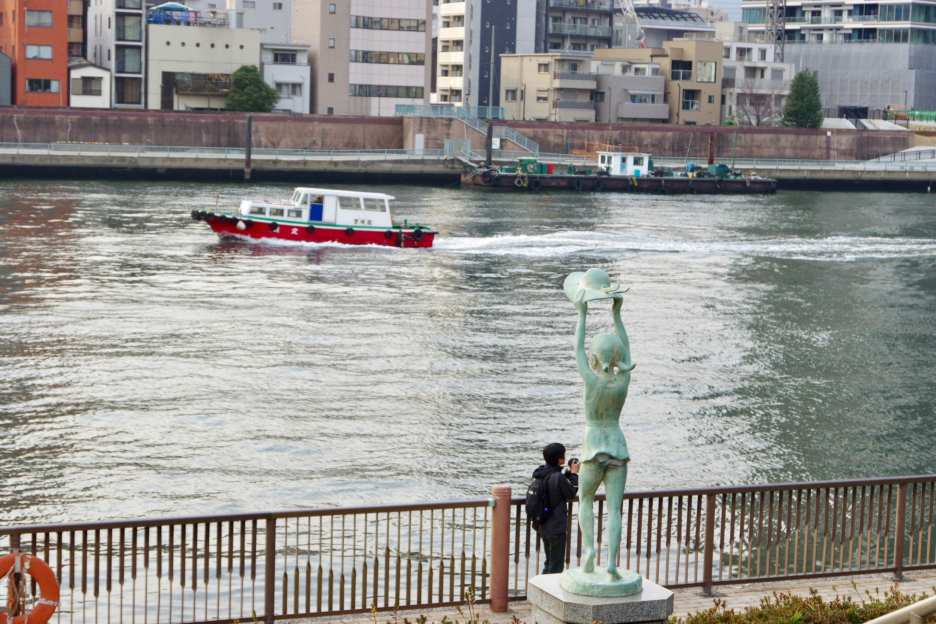 川の近くに立つ像とボートが通過する風景