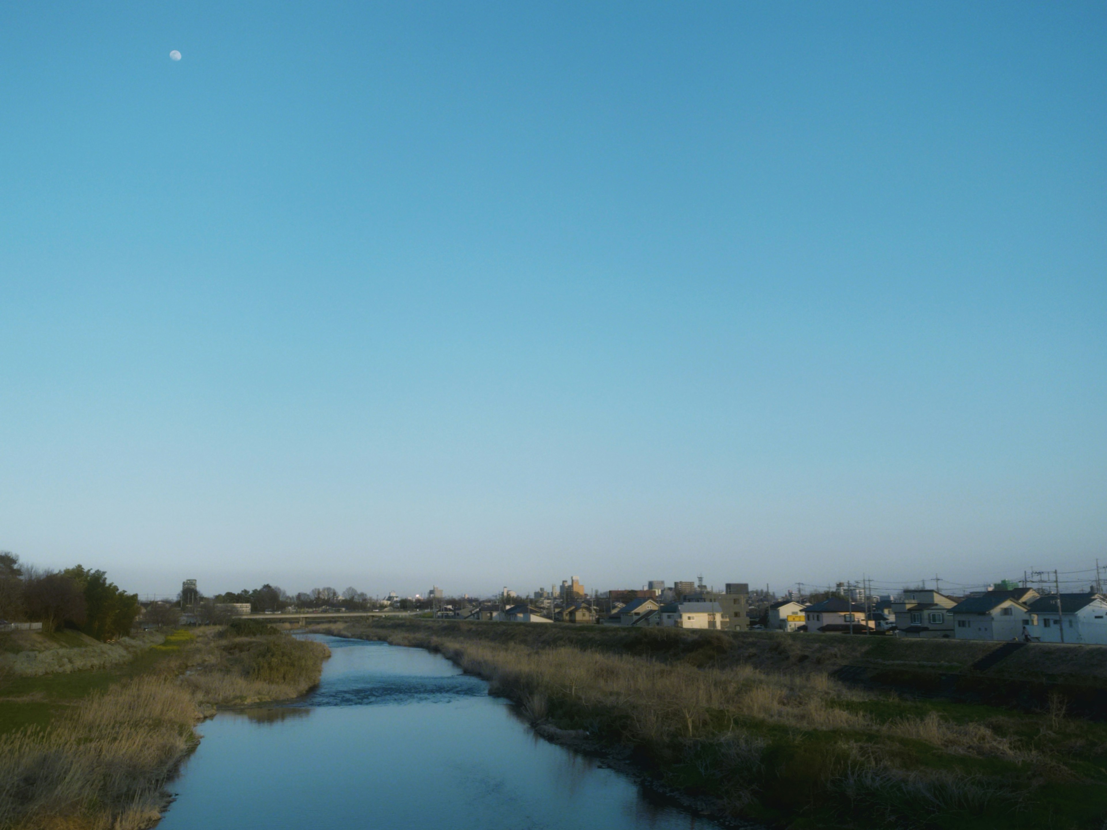 青空と川が広がり、住宅が見える静かな風景