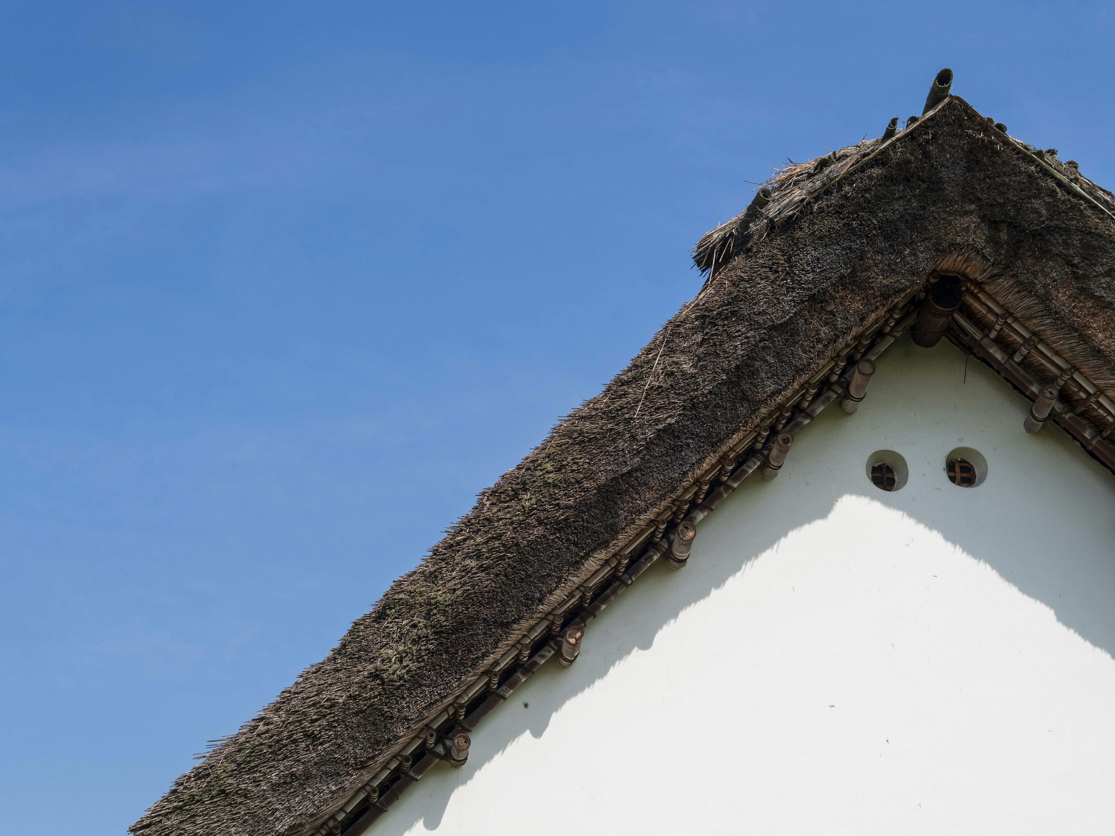 Ecke eines Reetdachs mit weißer Wand vor blauem Himmel