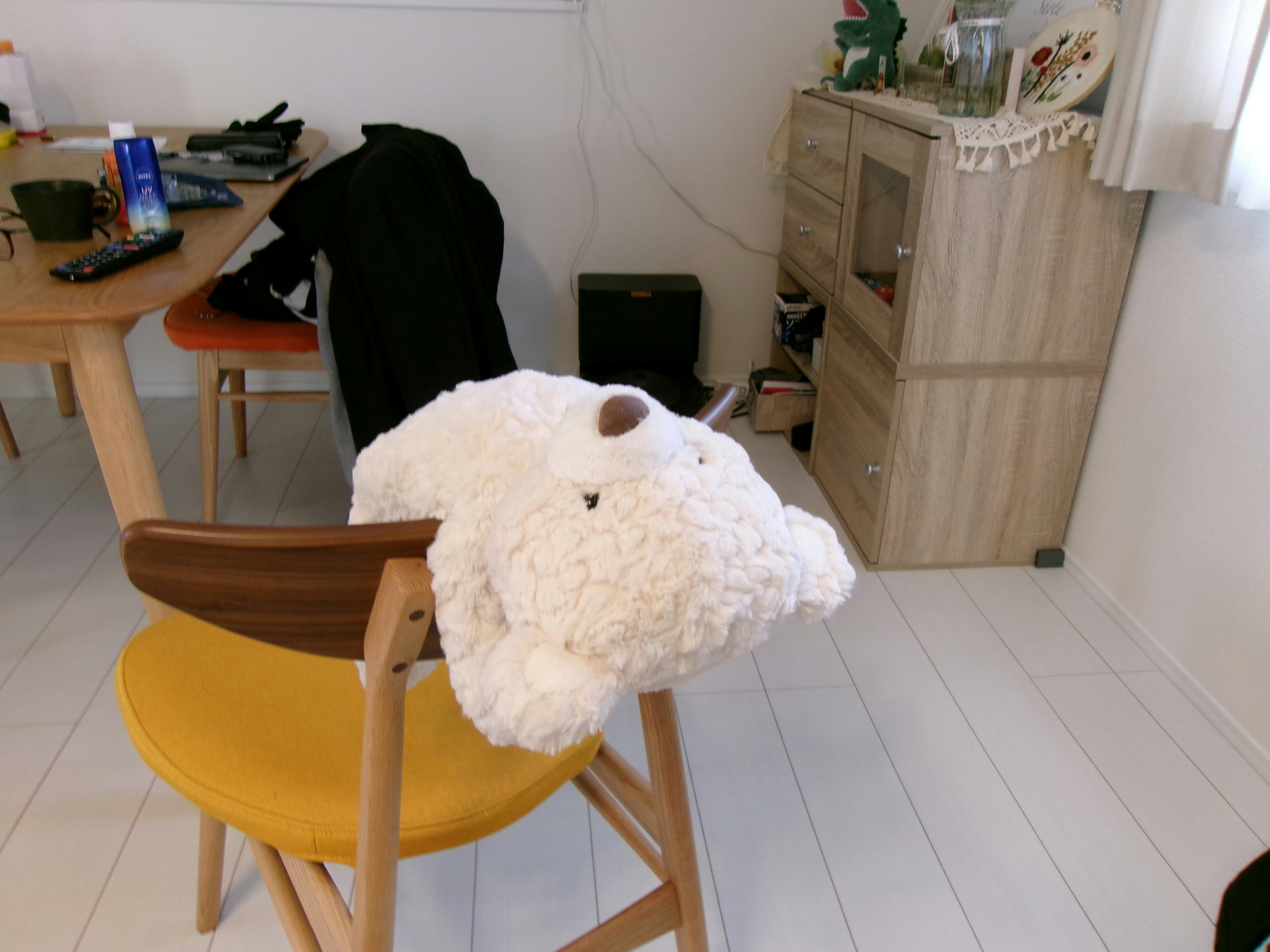 Un oso de peluche blanco en una silla de madera en una habitación luminosa