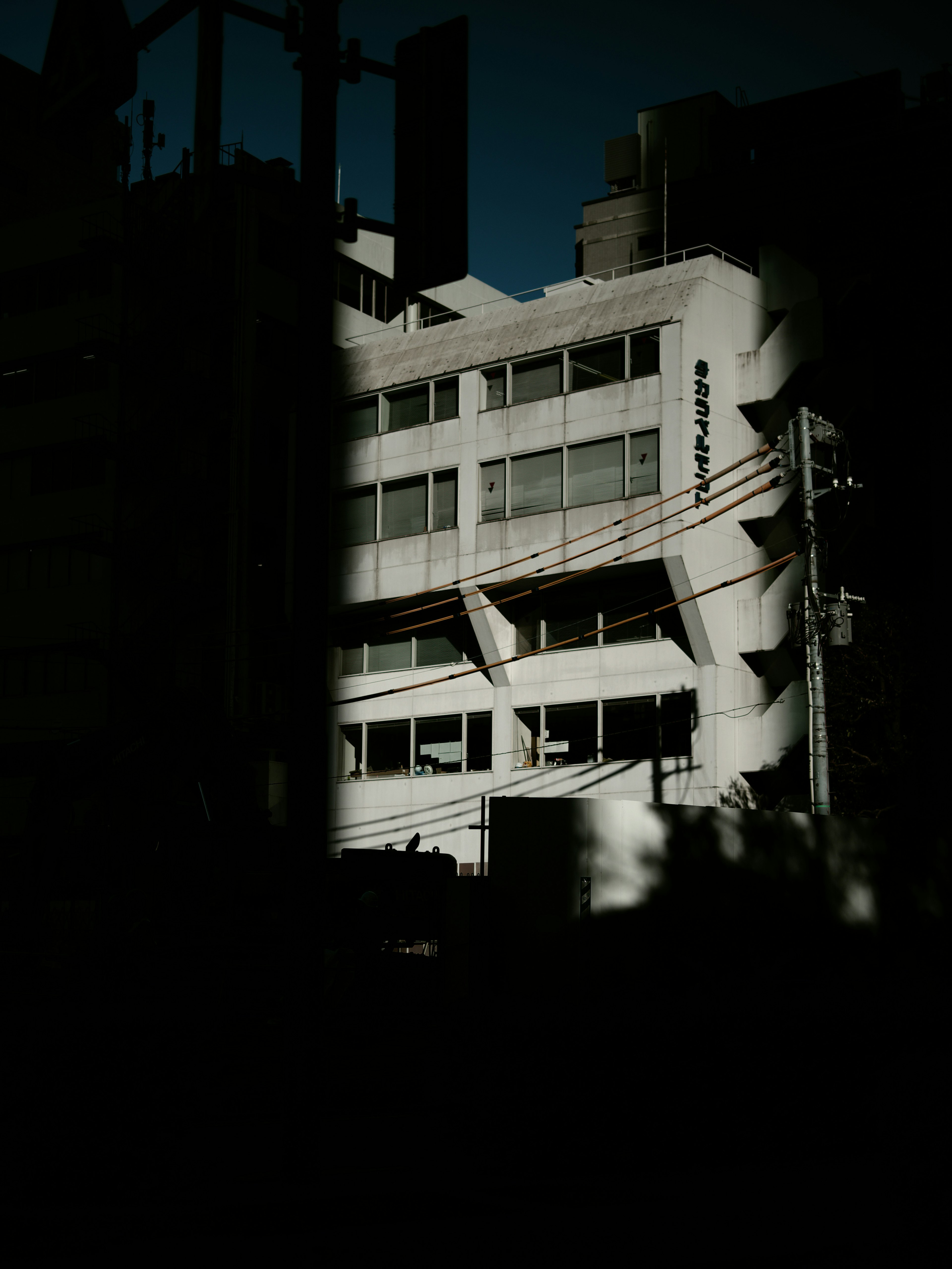 Edificio moderno parcialmente iluminado contra un fondo oscuro con líneas eléctricas