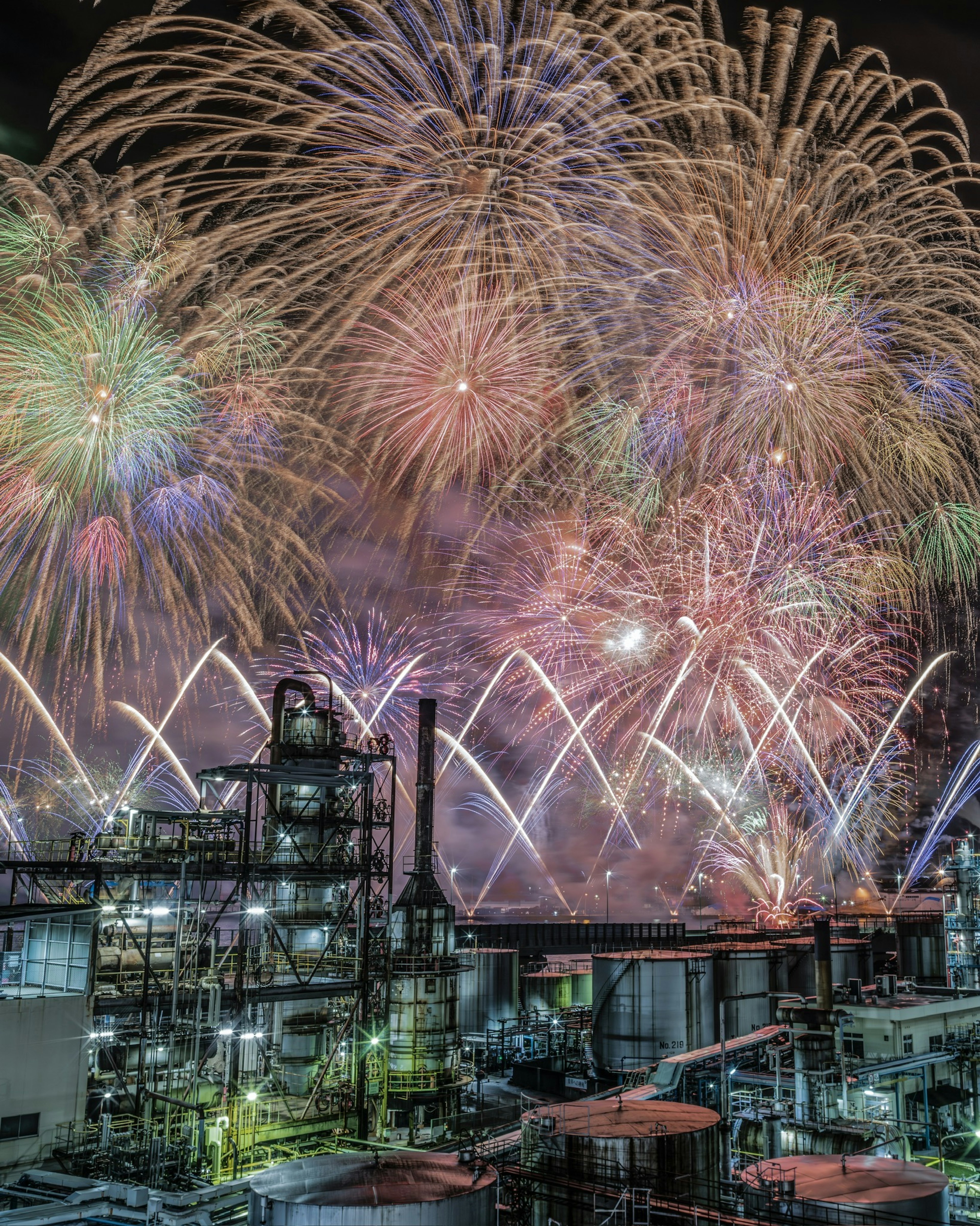 Colorful fireworks illuminate an industrial landscape at night