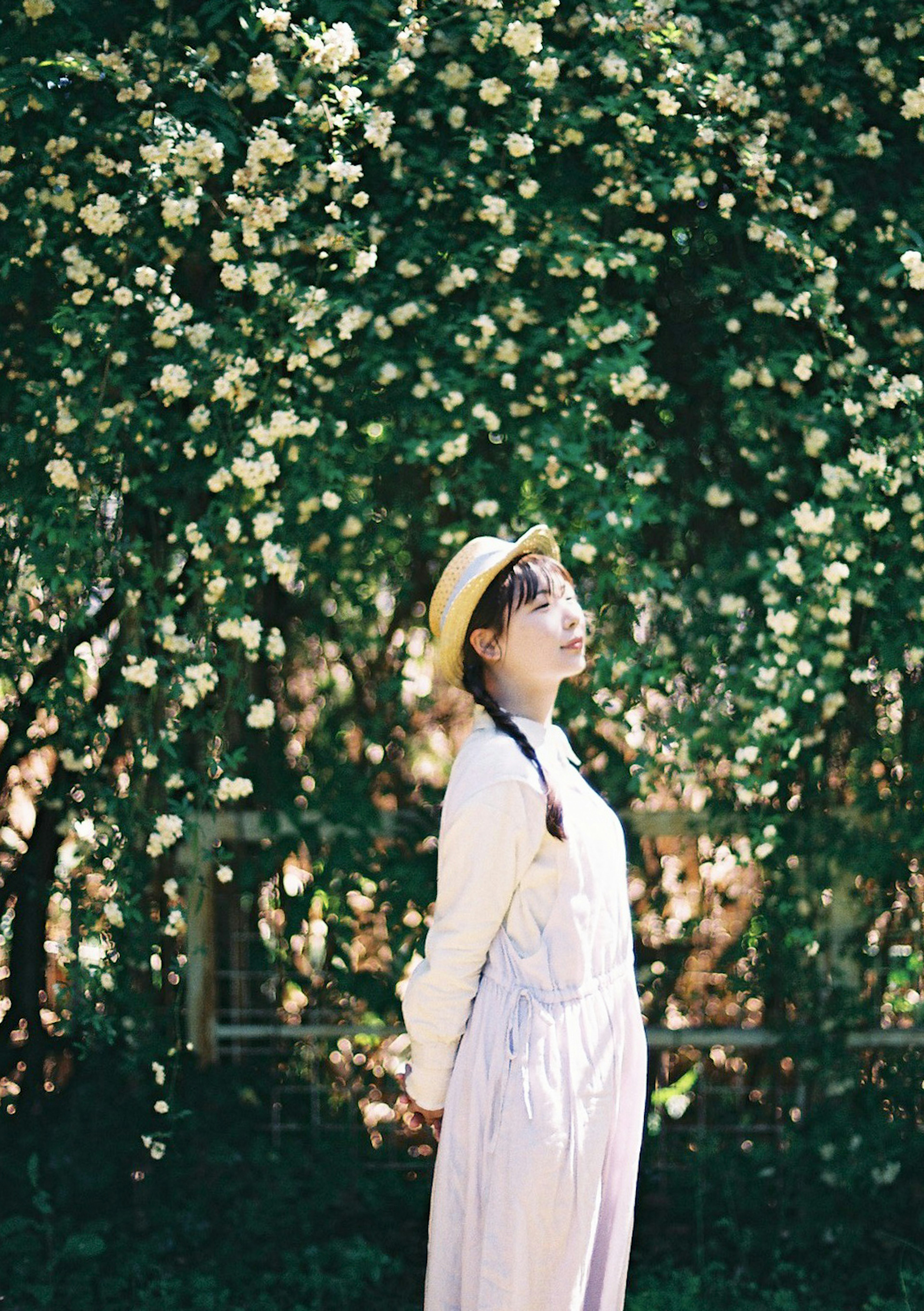 Girl in white dress wearing yellow hat standing against green floral background