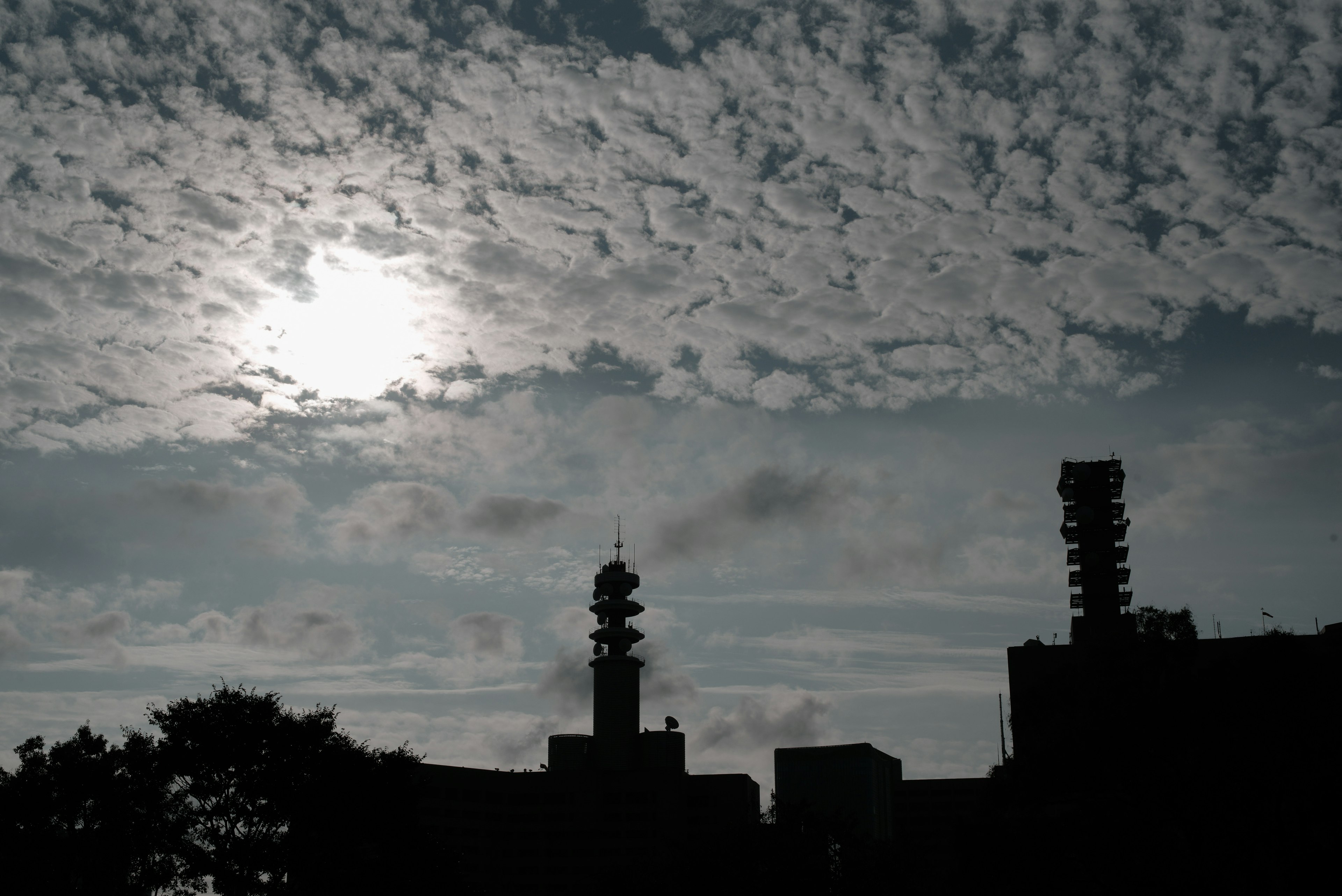 Silhouetten von Gebäuden vor einem bewölkten Himmel mit der Sonne, die durchscheint