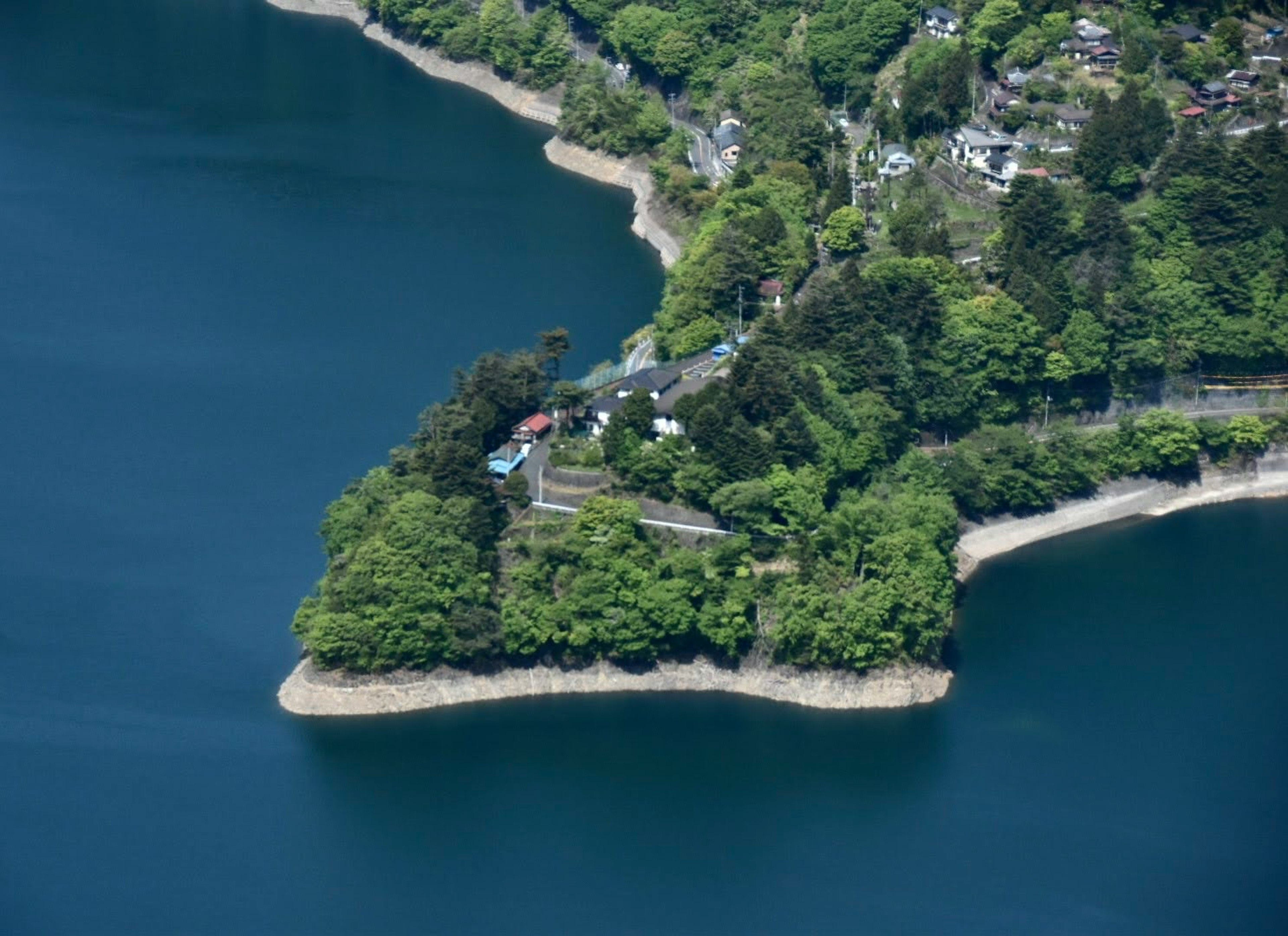 Une maison et un jardin situés sur une péninsule verte entourée d'un lac bleu