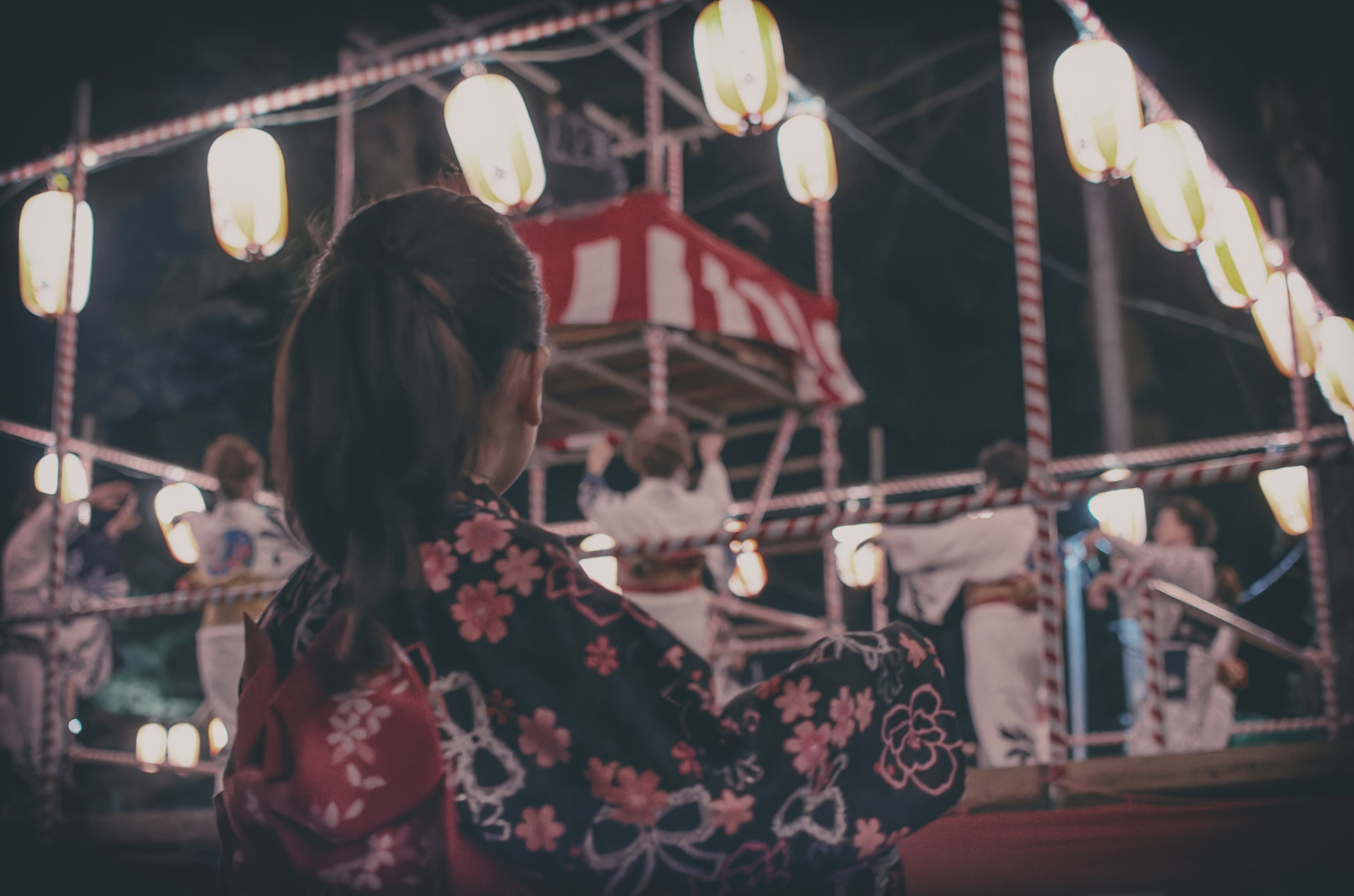 A girl in a kimono watching a dance at a night festival