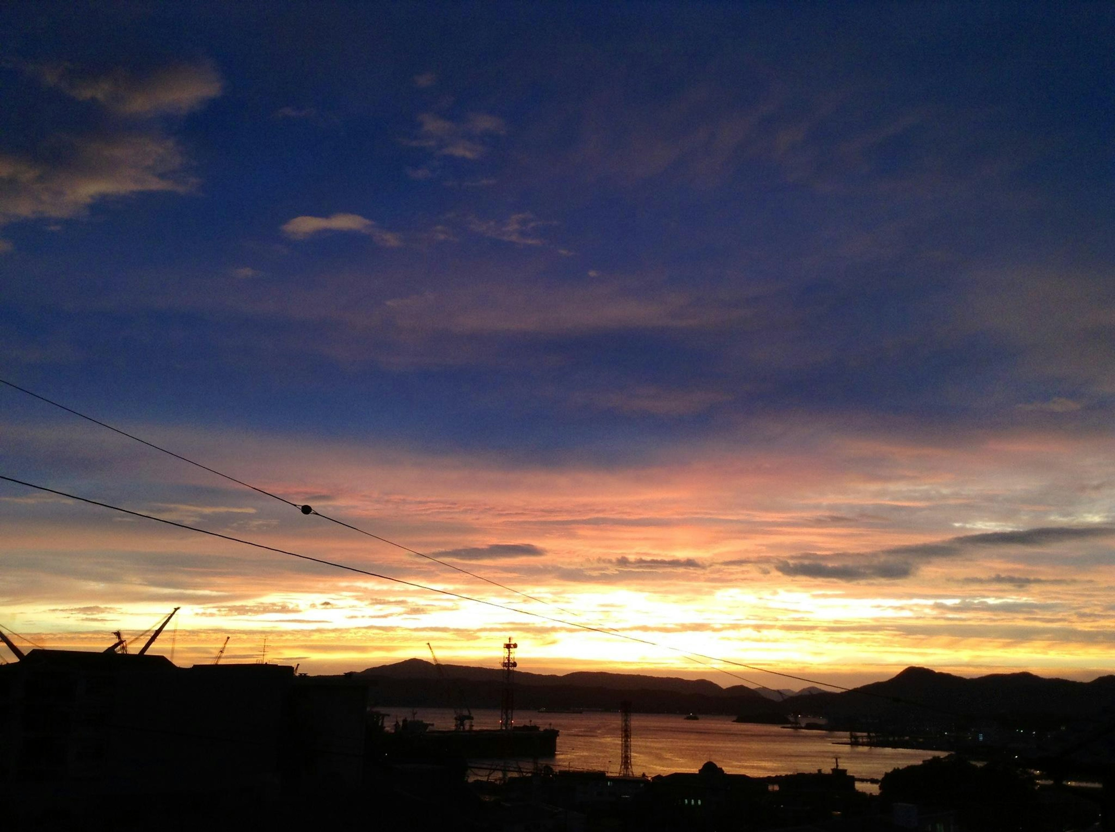 Ciel de coucher de soleil vibrant sur l'océan avec des silhouettes de collines