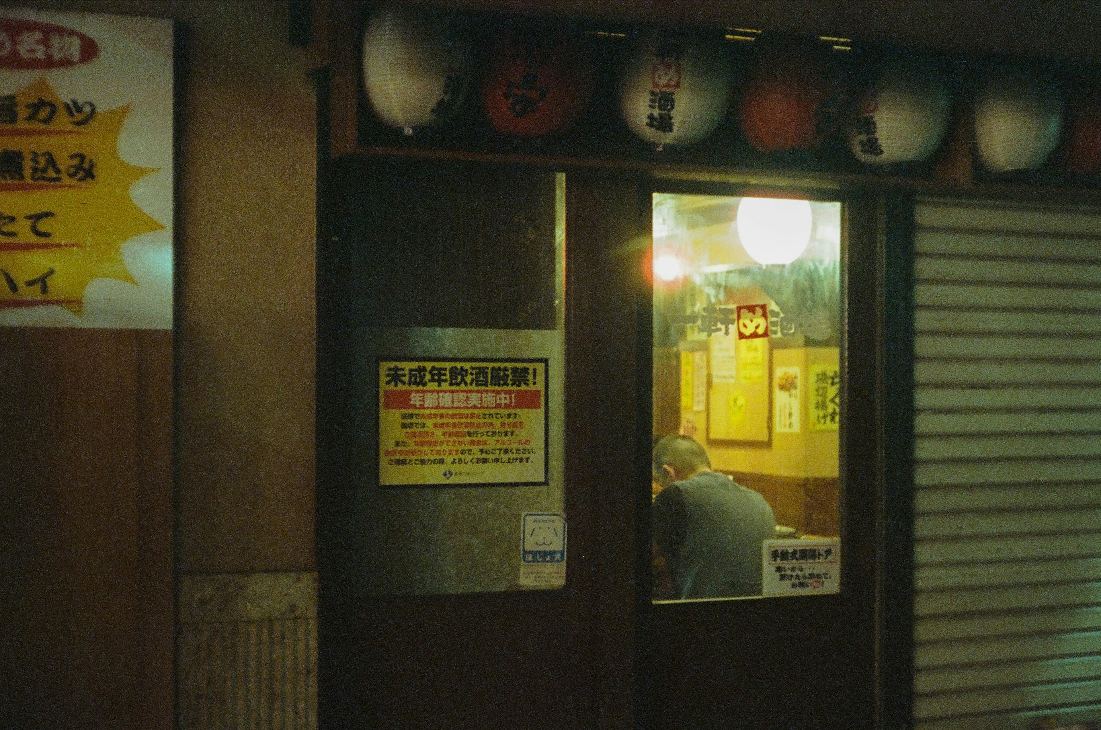 Exterior de un izakaya japonés de noche con ventana iluminada y linternas