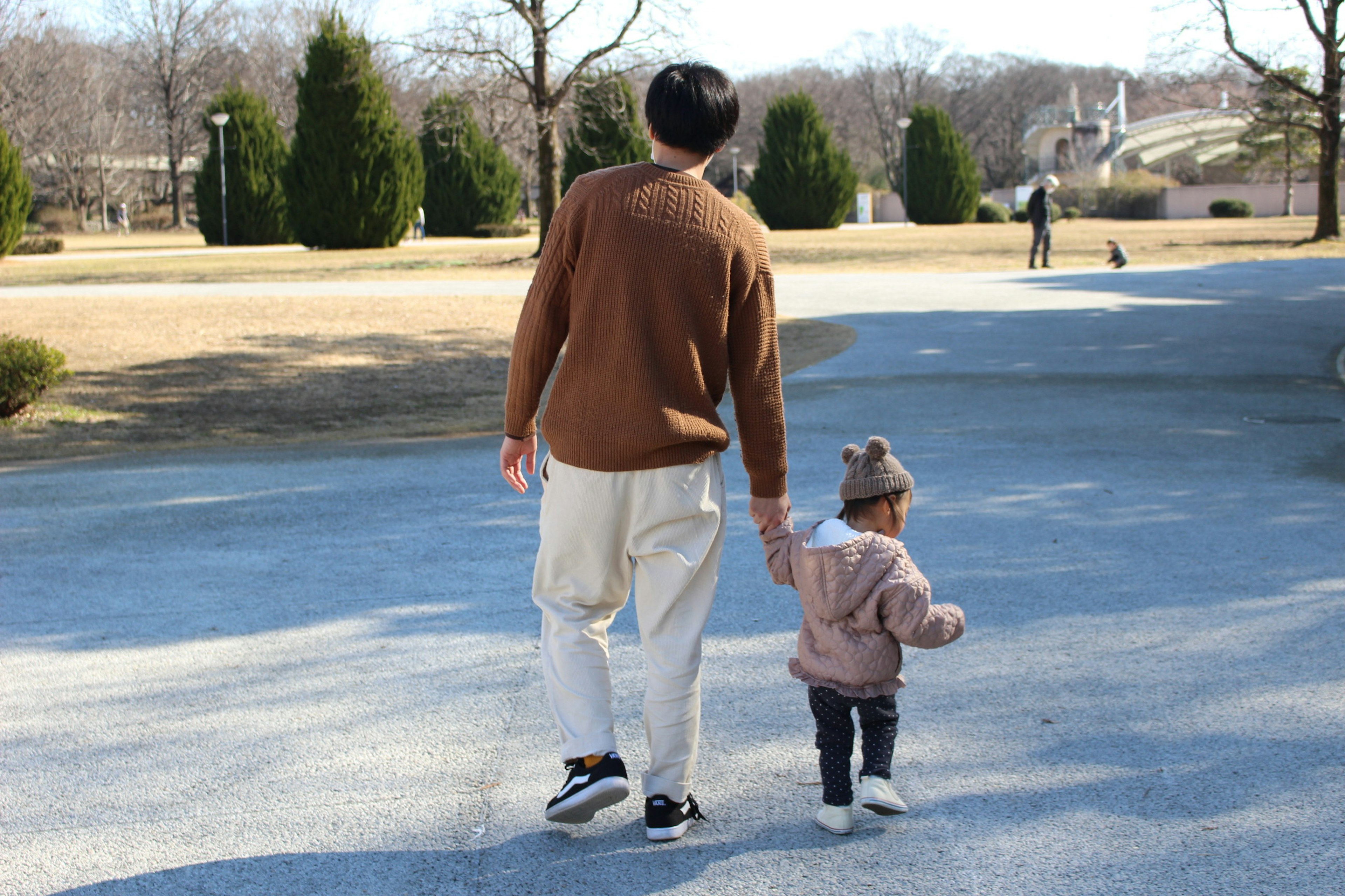 Un parent et un enfant marchant dans un parc avec de grands arbres et de l'herbe ouverte