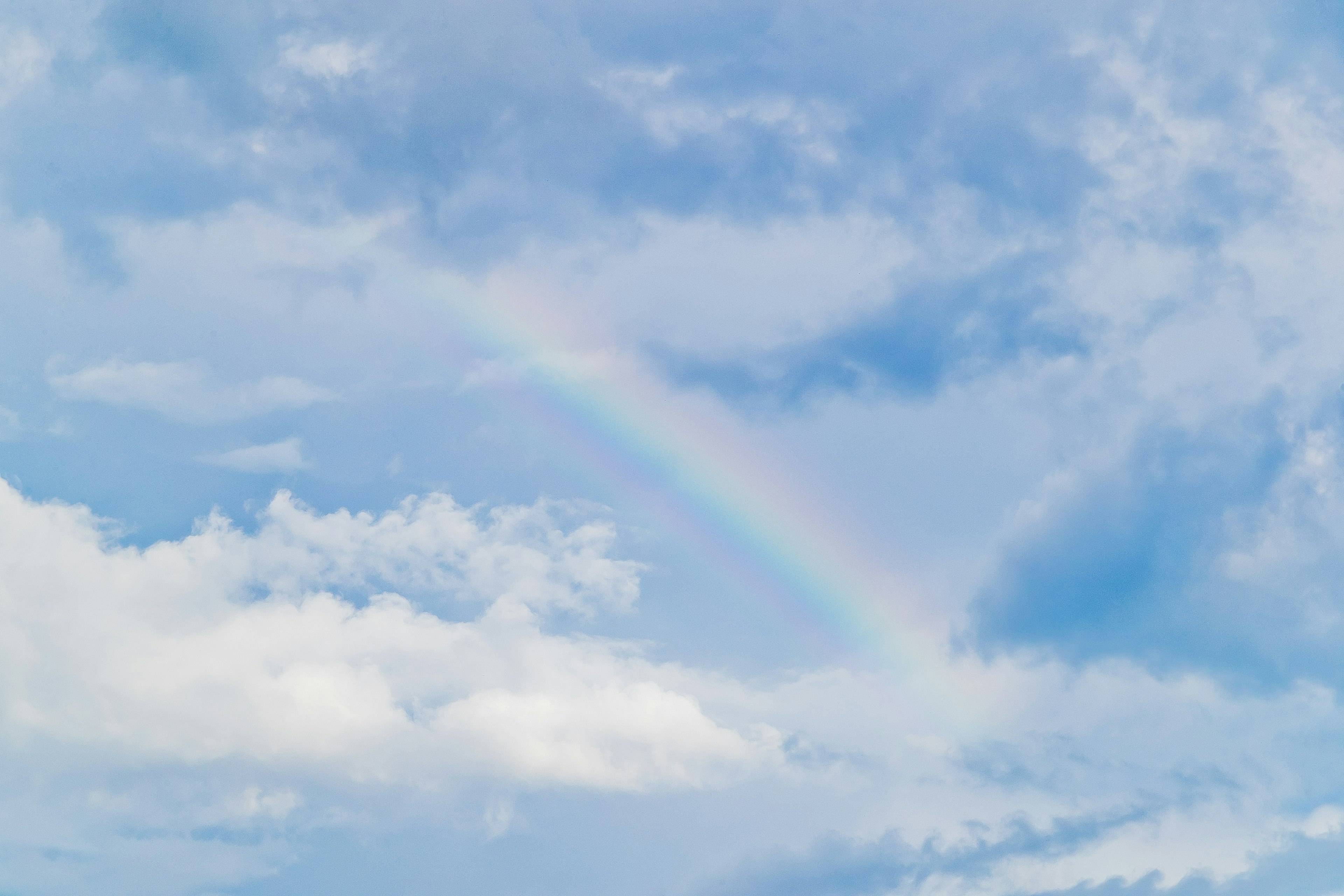 Faint rainbow arching across a blue sky with white clouds