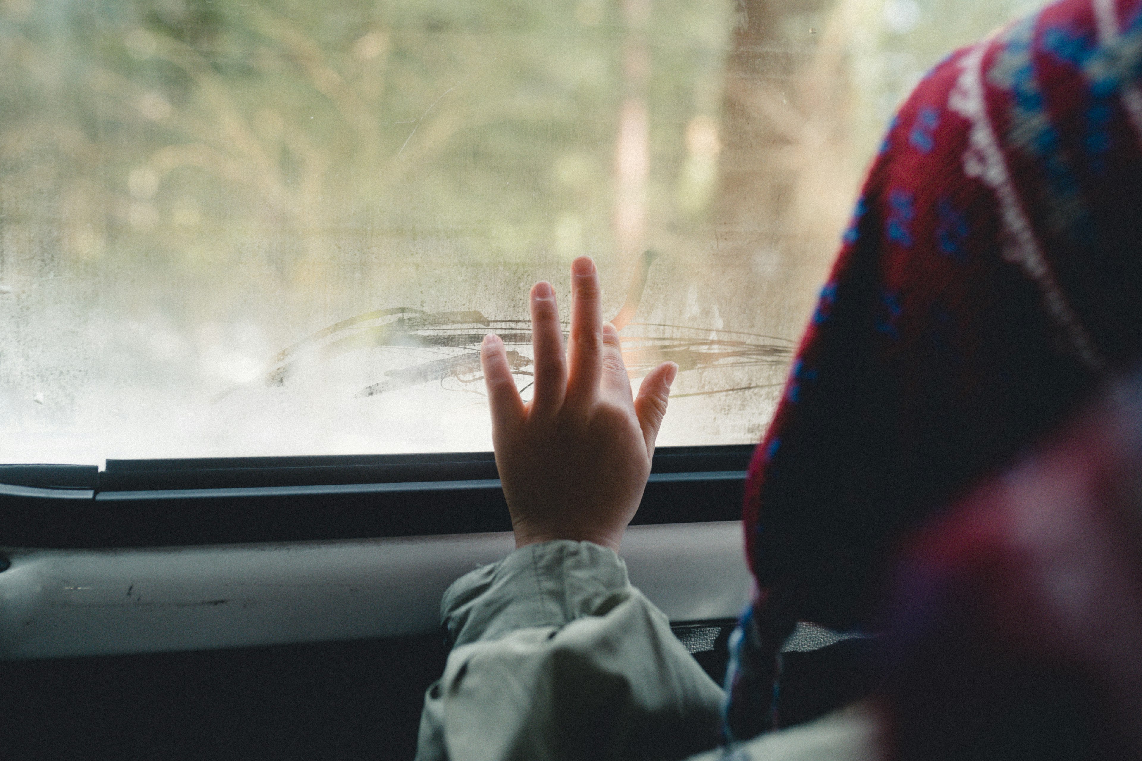 Mano di un bambino su un finestrino appannato con un maglione colorato