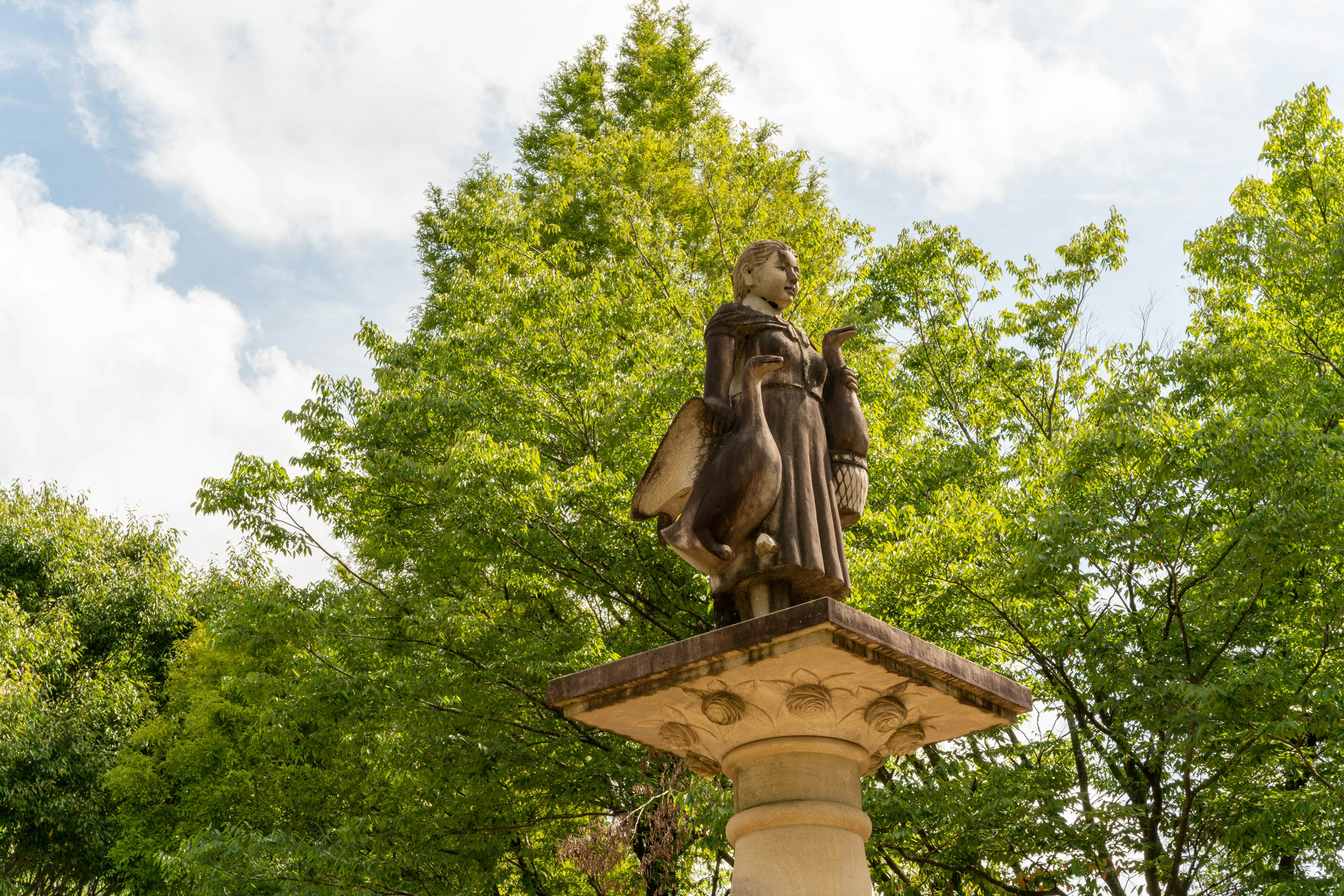 Une statue se dresse parmi des arbres verts luxuriants sous un ciel nuageux serein