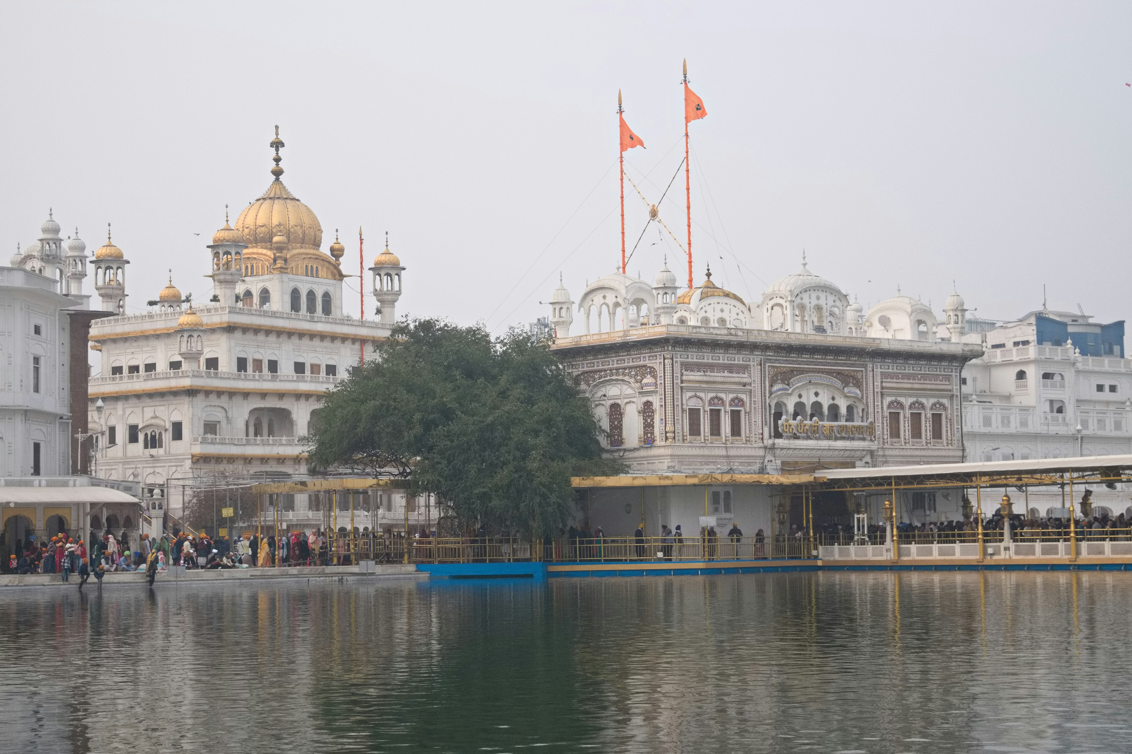 Blick auf den Goldenen Tempel mit einem ruhigen Wasser und aufwendiger Architektur mit einer goldenen Kuppel und orangefarbenen Fahnen