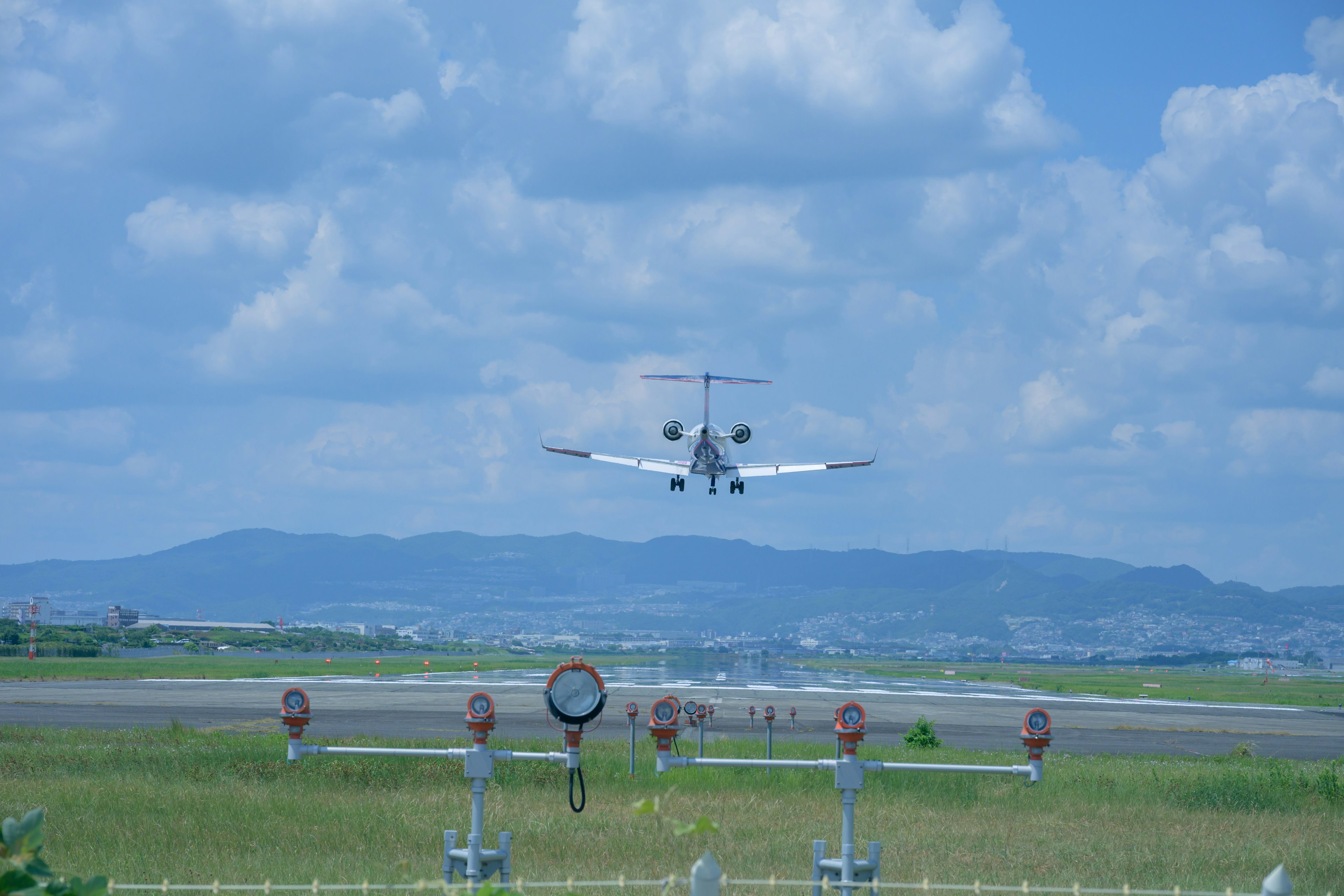 Piccolo aereo in atterraggio su una pista d'aeroporto con cielo blu chiaro e nuvole