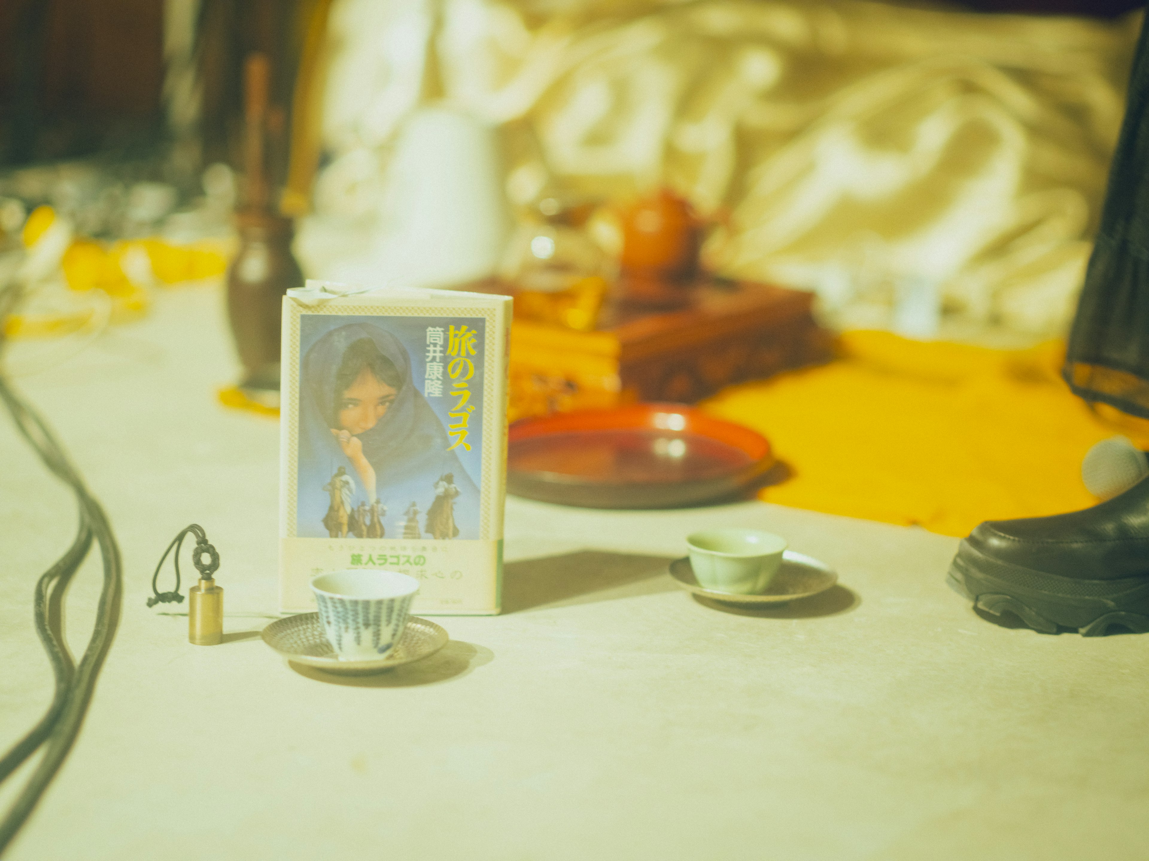 Image d'une petite tasse à thé et d'une couverture de livre sur une table avec un tissu à motifs et des objets décoratifs en arrière-plan