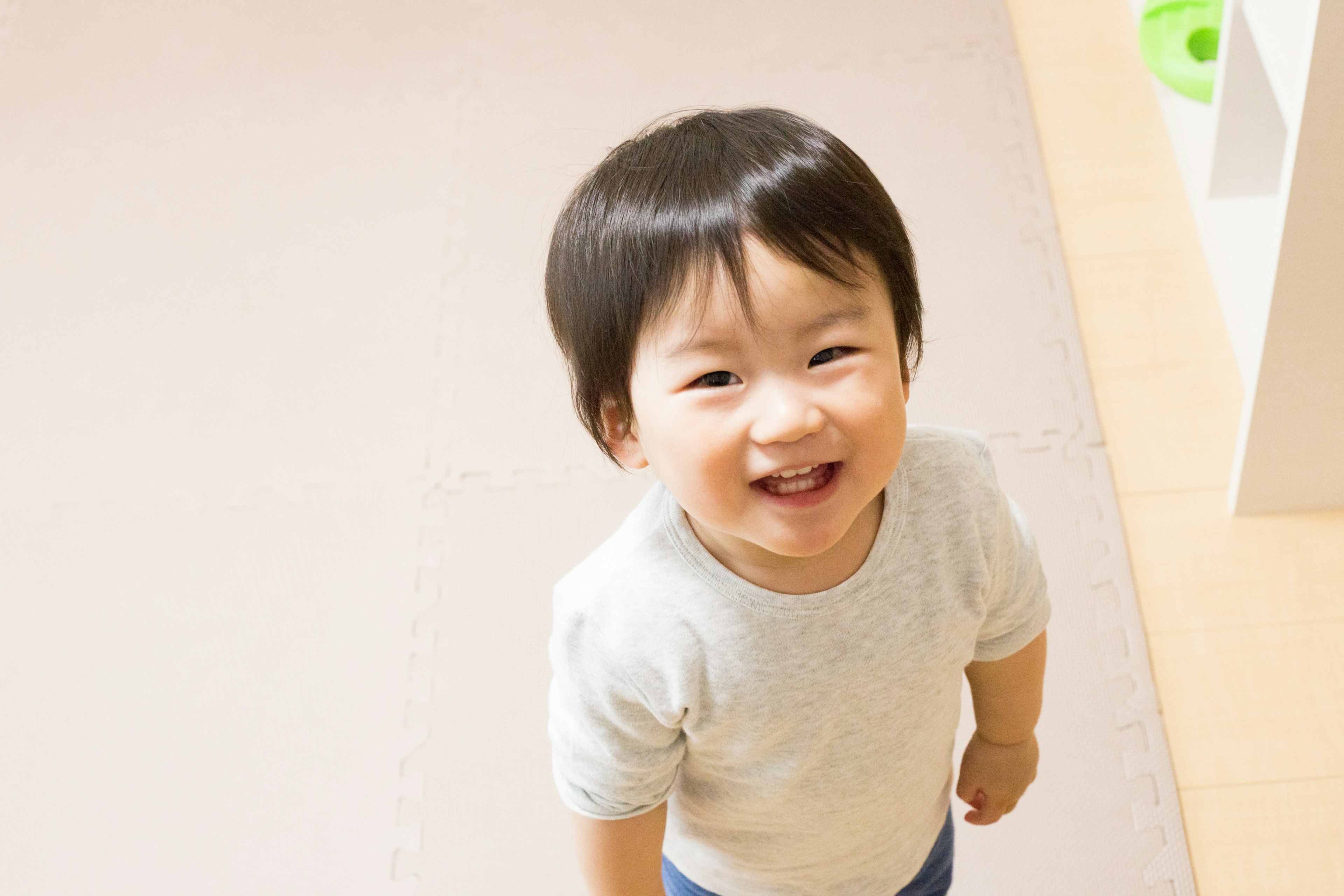 A smiling toddler looking up at the camera in a room