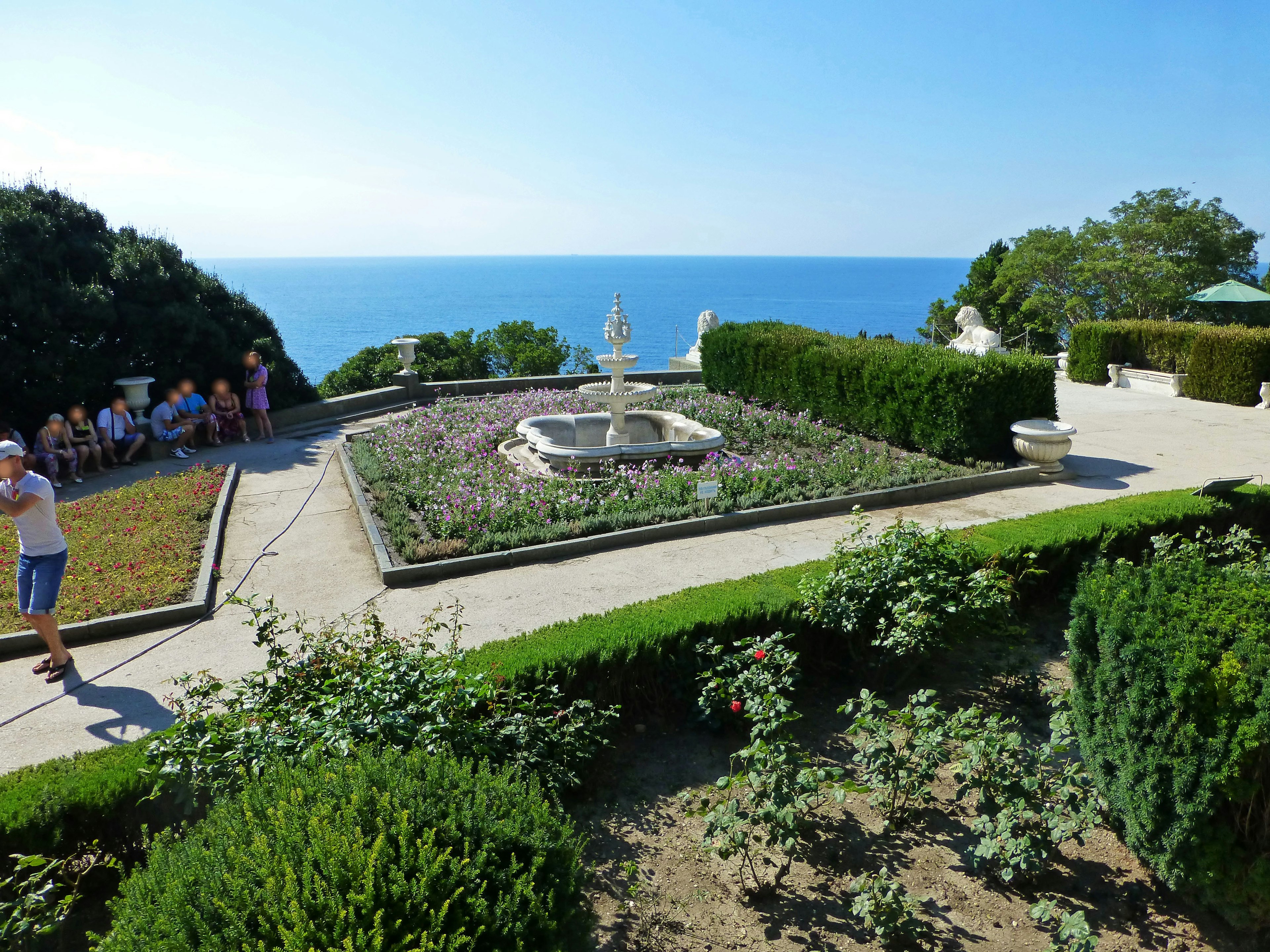 Hermoso jardín con fuente con vista al mar con plantas y visitantes