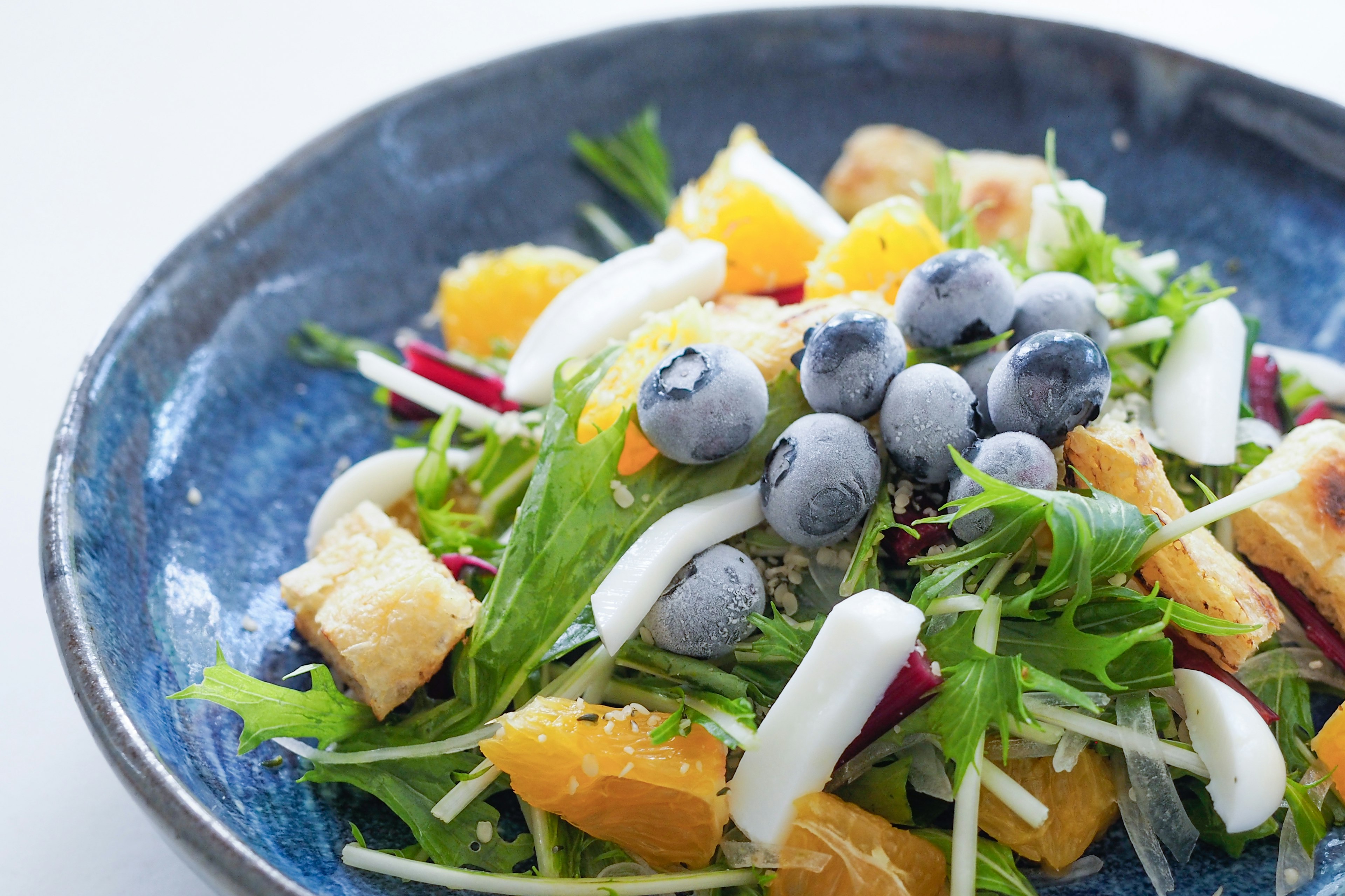 青い皿に盛られたサラダ色とりどりのフルーツと野菜が特徴