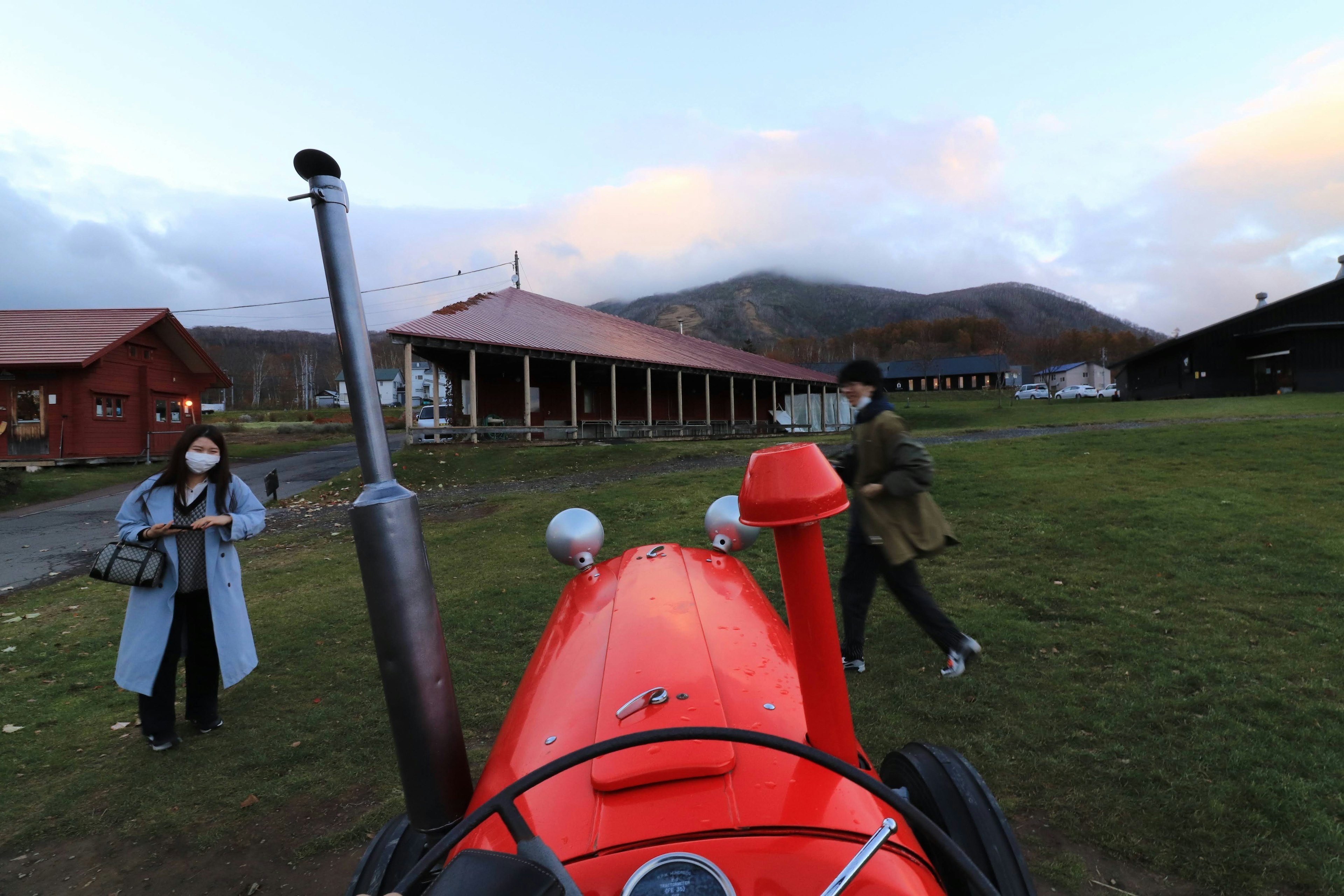 Dos personas cerca de un tractor rojo con montañas al fondo