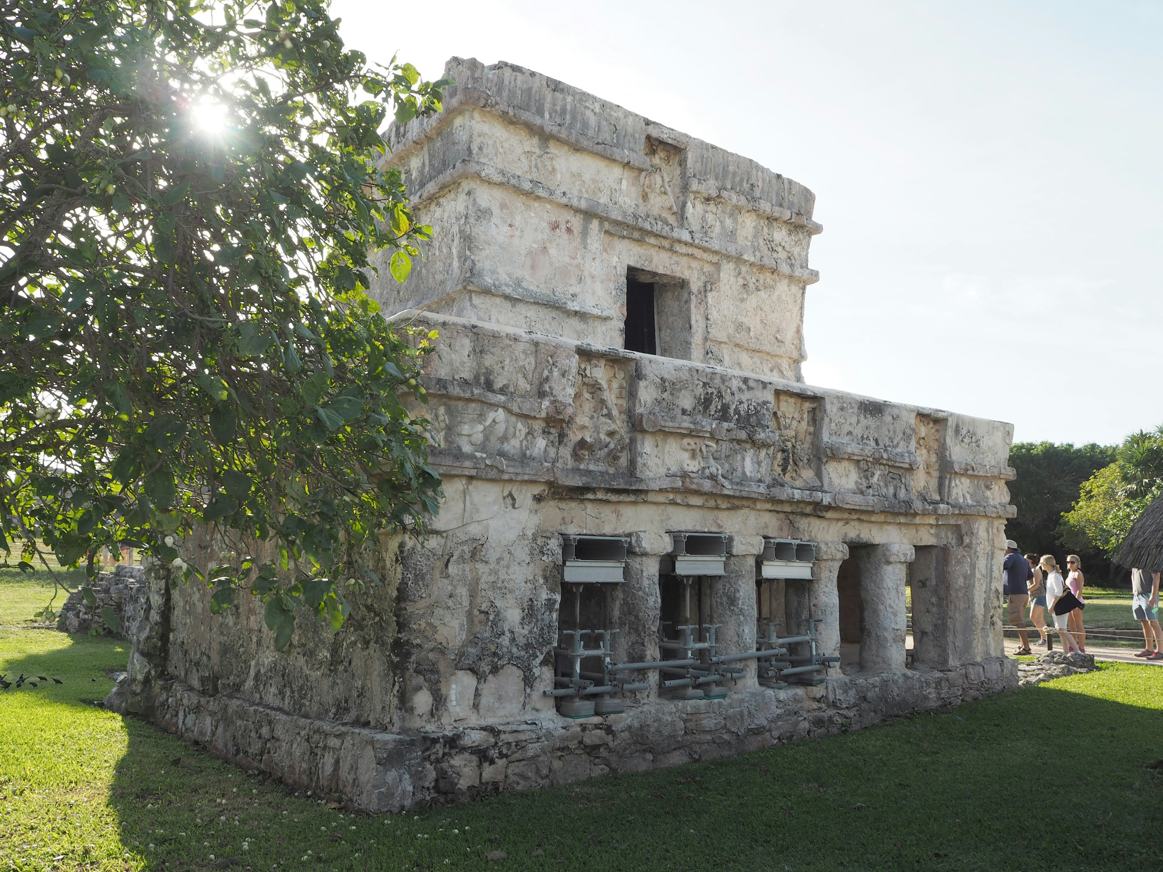 Seitenansicht eines kleinen Steingebäudes aus der alten Maya-Zivilisation umgeben von Grünflächen