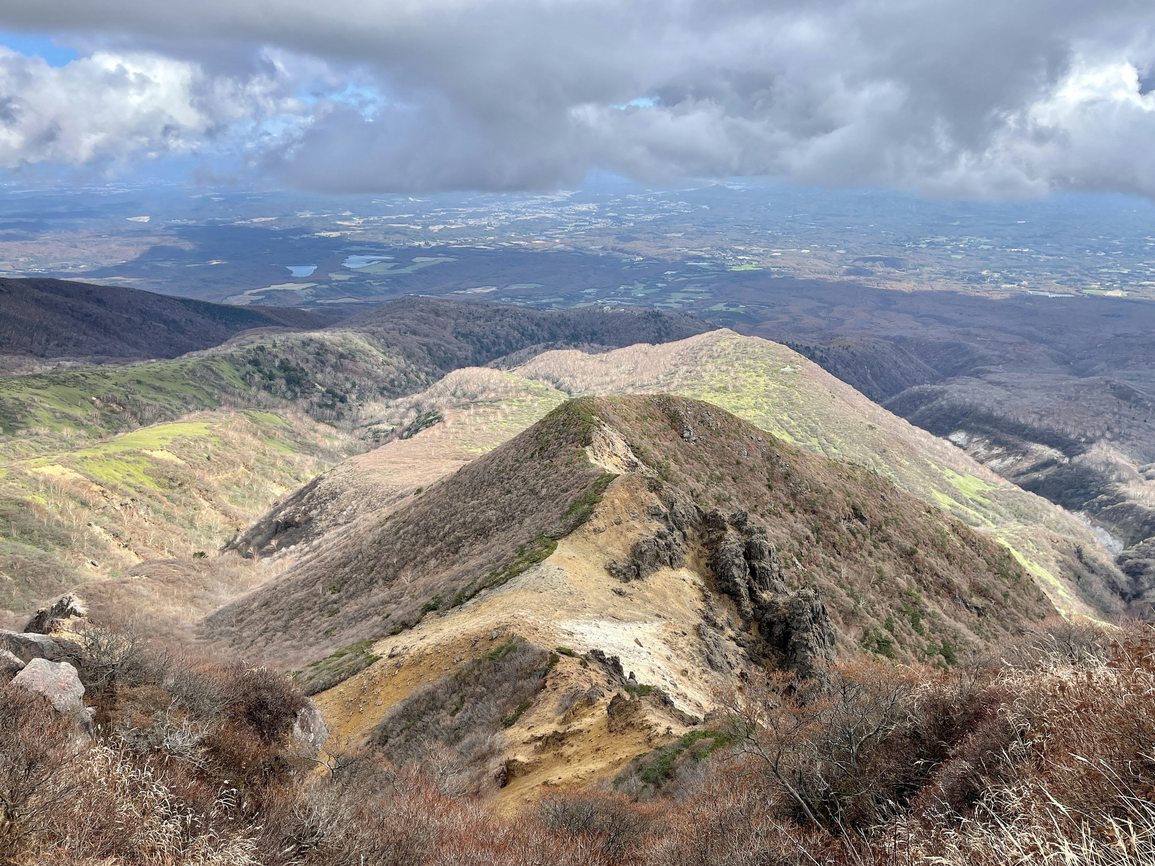 Vista panoramica da una cima montuosa con pendii verdi e marroni sotto un cielo nuvoloso