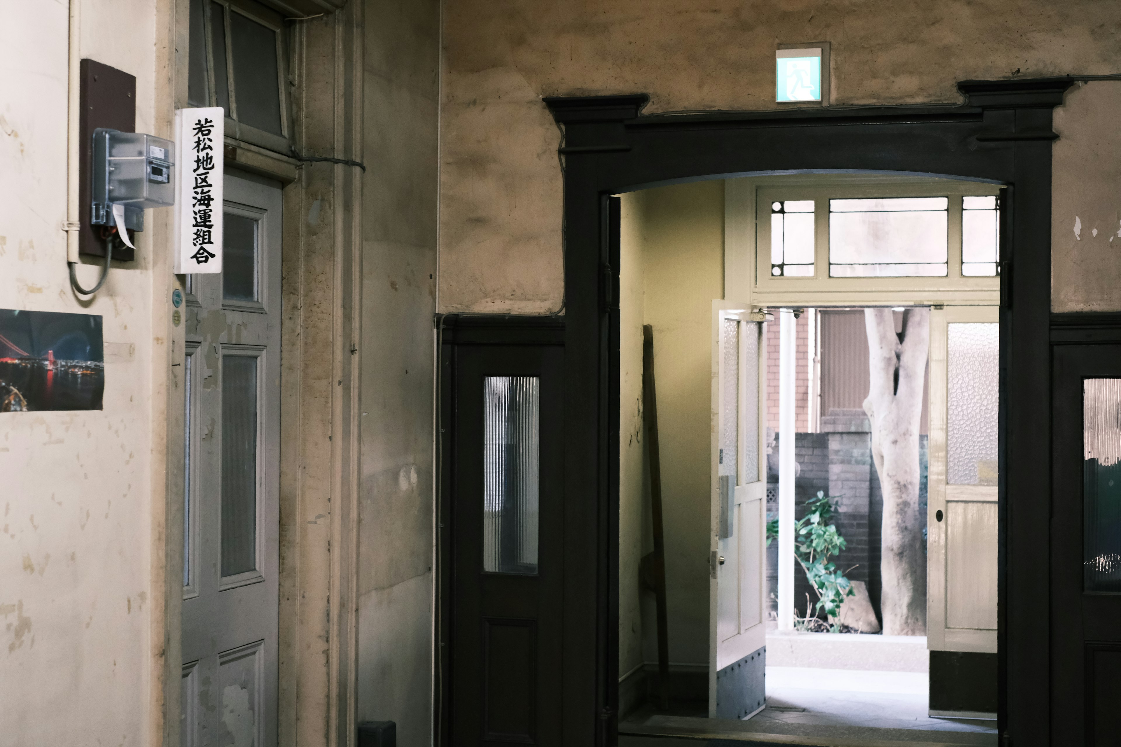 Corridoio interno di un vecchio edificio con un telefono sul muro e luce che filtra dalle finestre