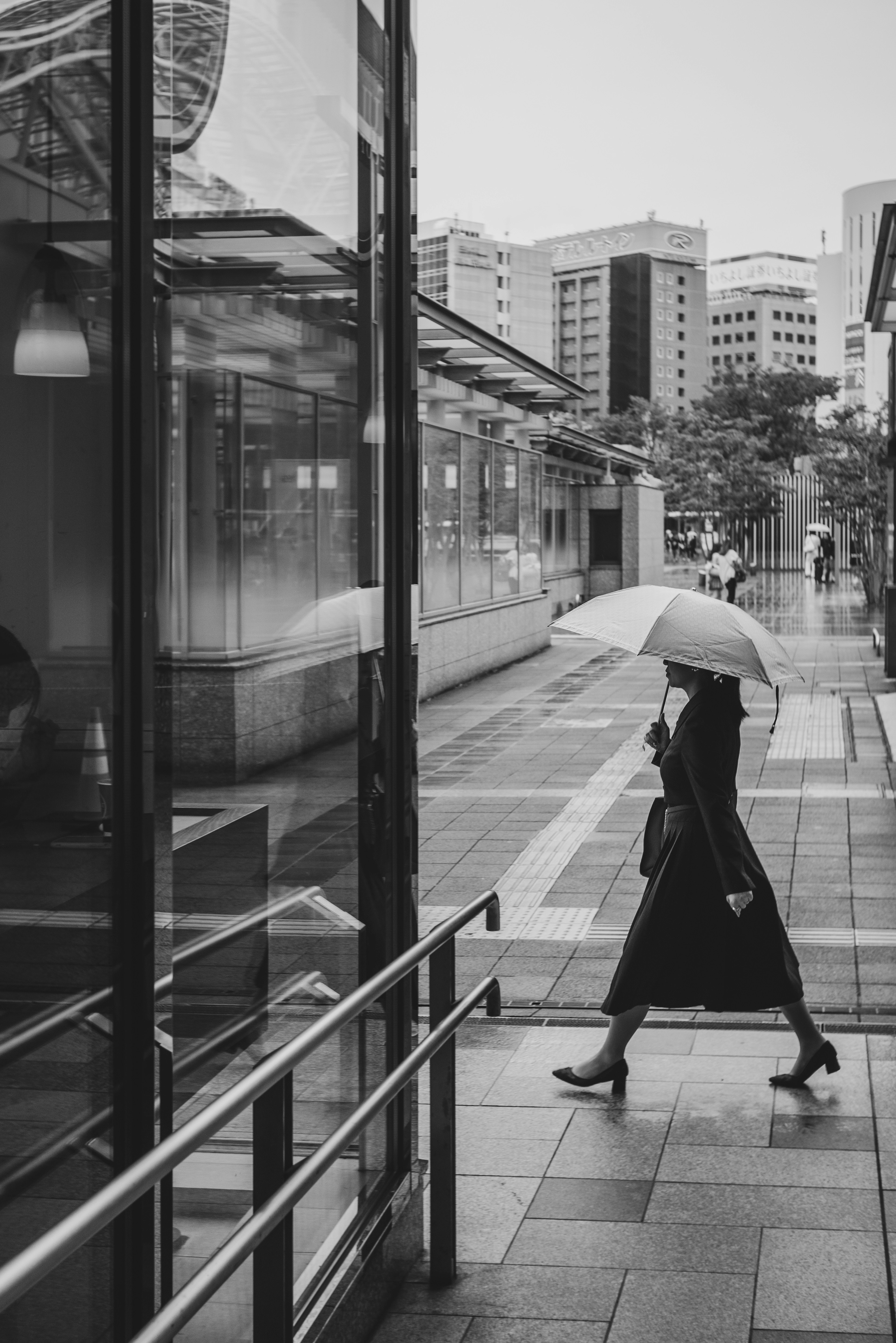 黒いコートを着た女性が傘を持って歩いている街の風景