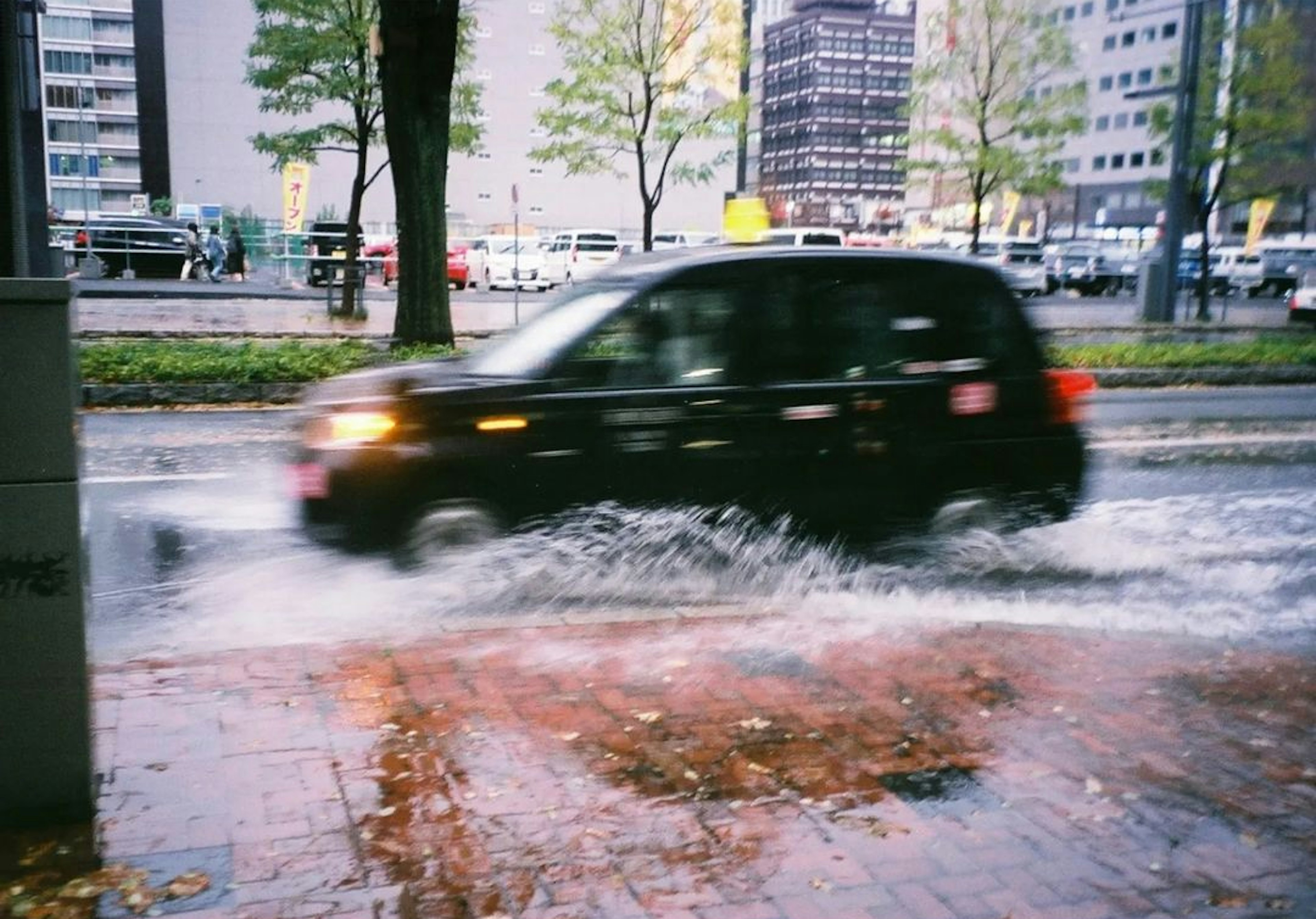 雨の中を走る黒い車と水たまり