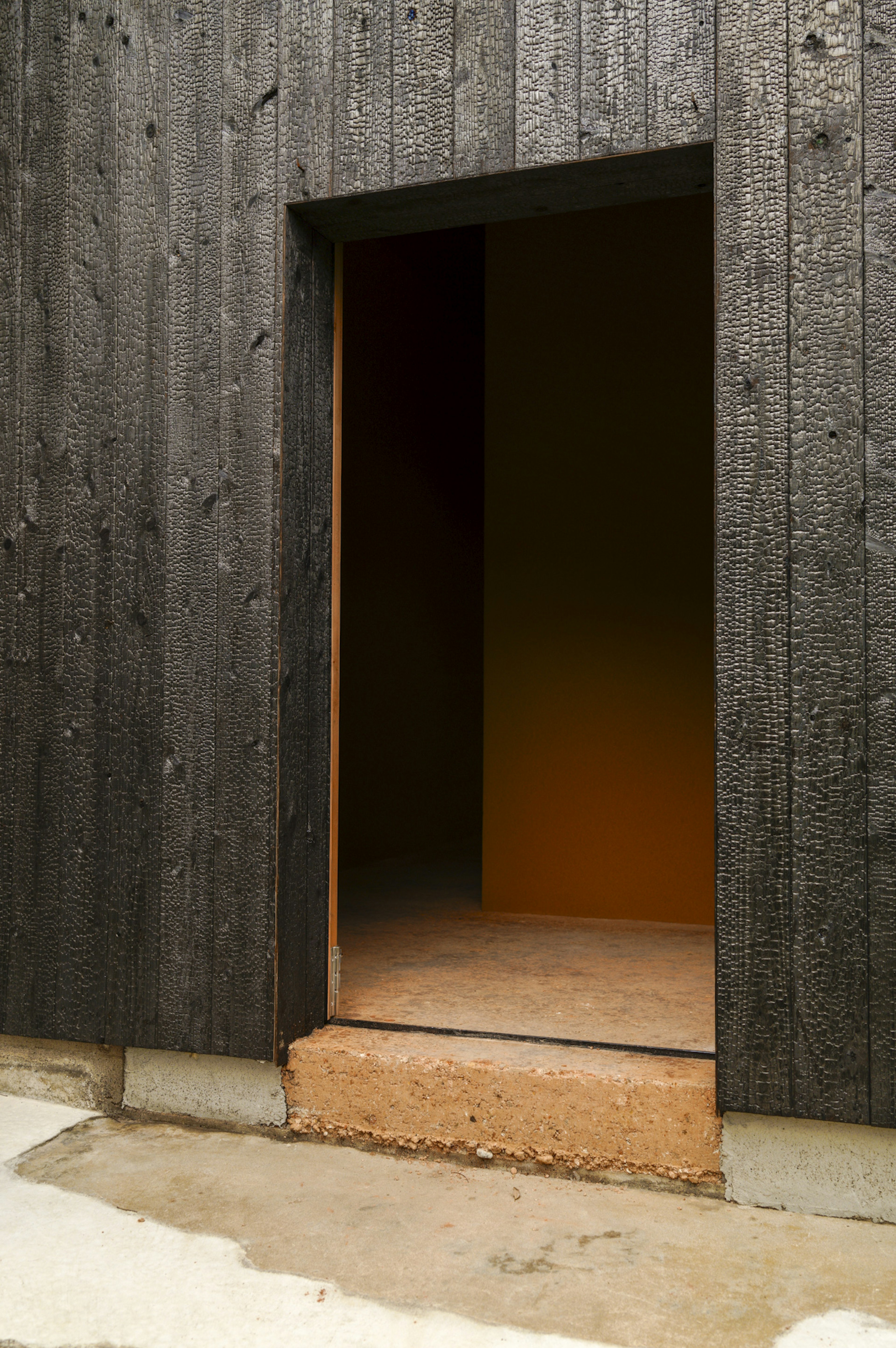 Puerta abierta en una pared de madera negra con luz naranja iluminando el interior