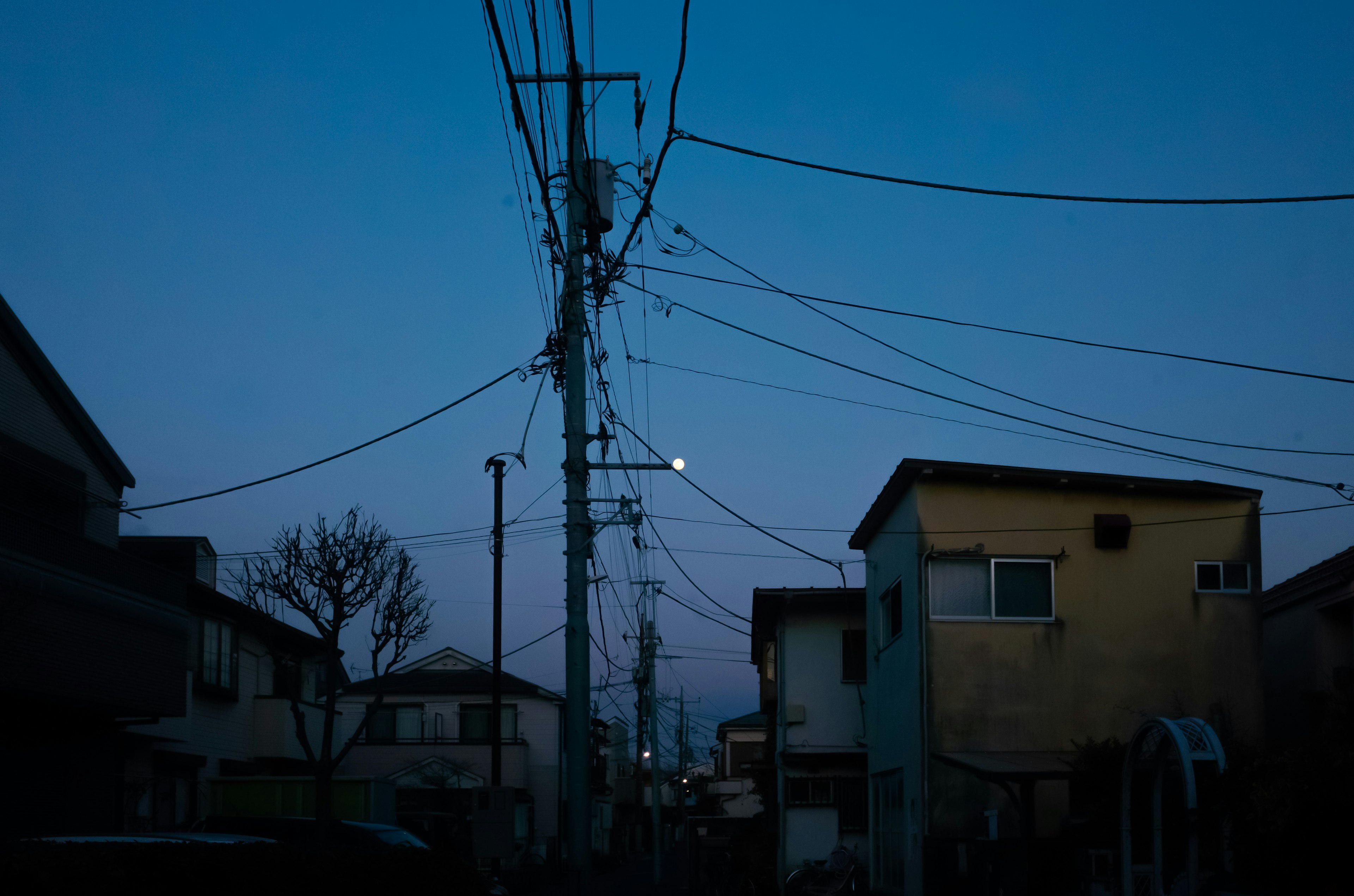 Escena de calle residencial al anochecer Líneas eléctricas cruzando el vecindario Luna llena en el cielo nocturno