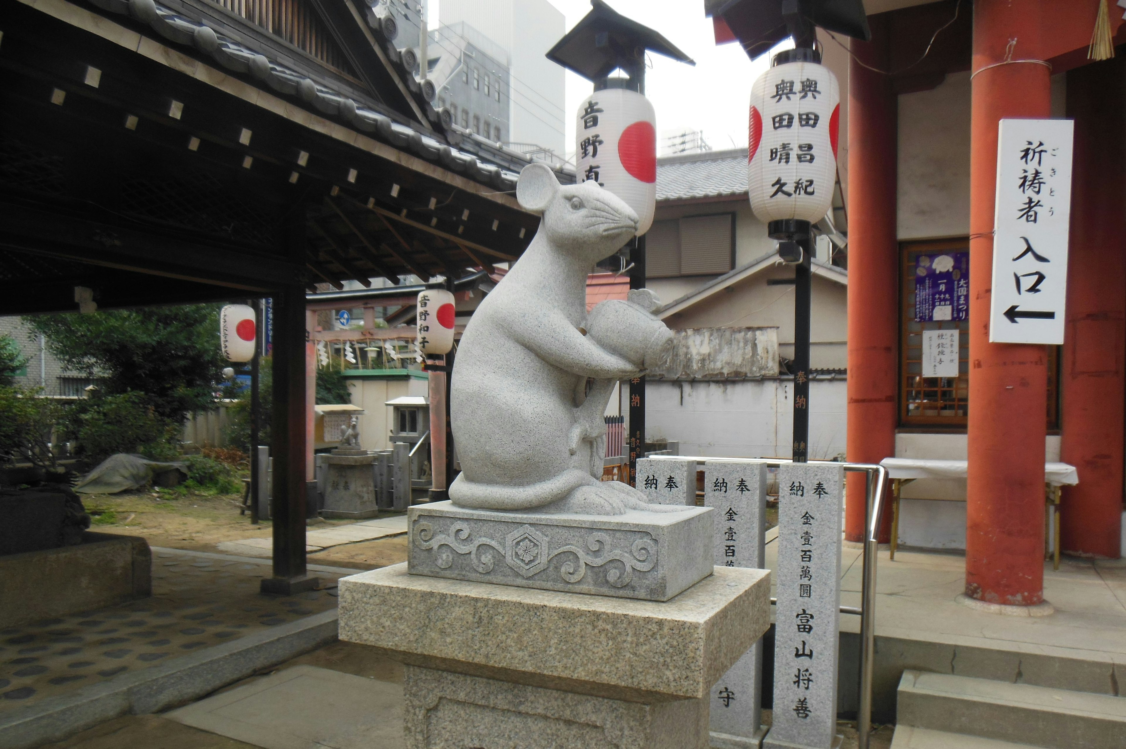 A white rabbit sculpture at a shrine with red lanterns and buildings in the background