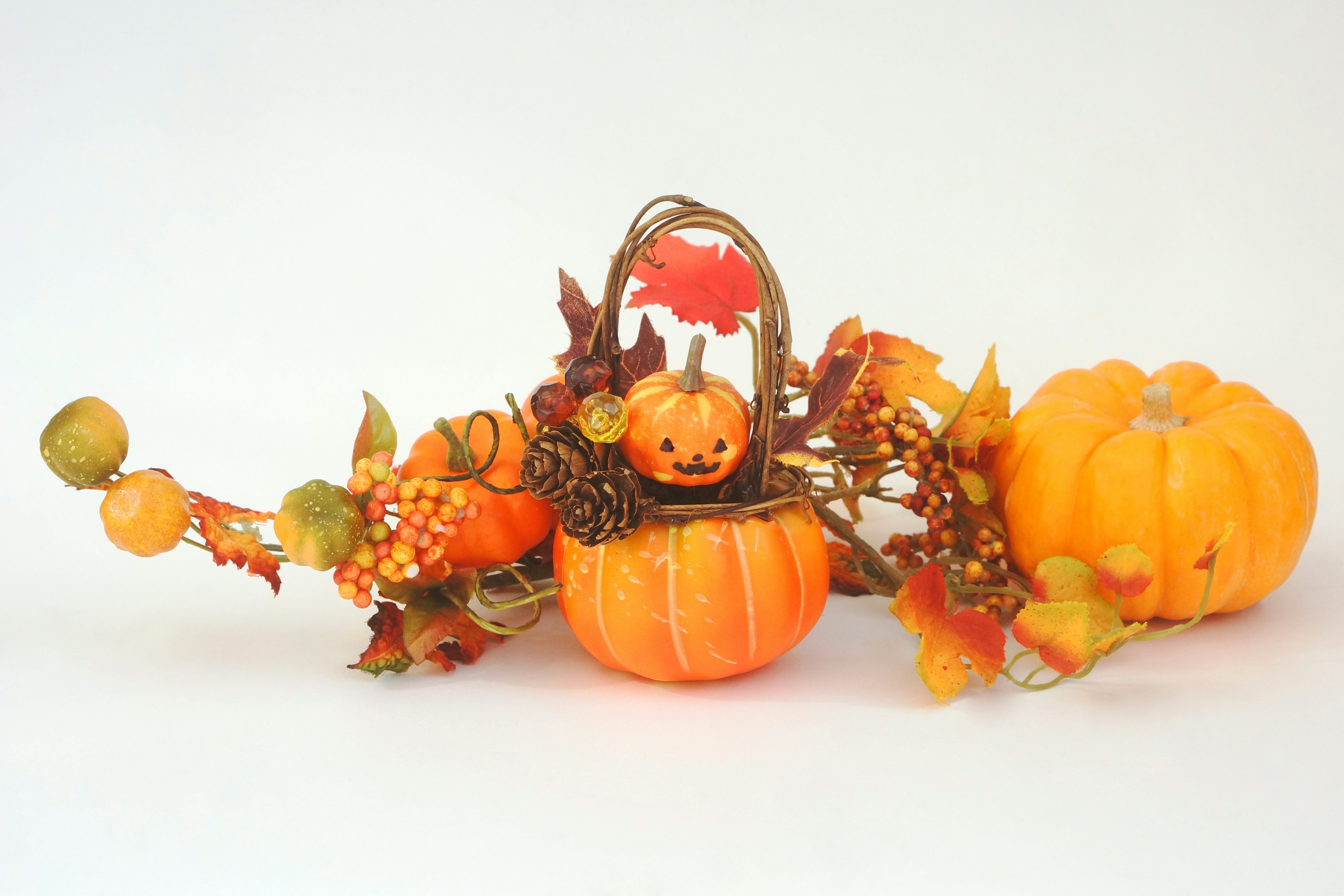 Una pequeña cesta con una calabaza sonriente rodeada de hojas de otoño y dos calabazas naranjas