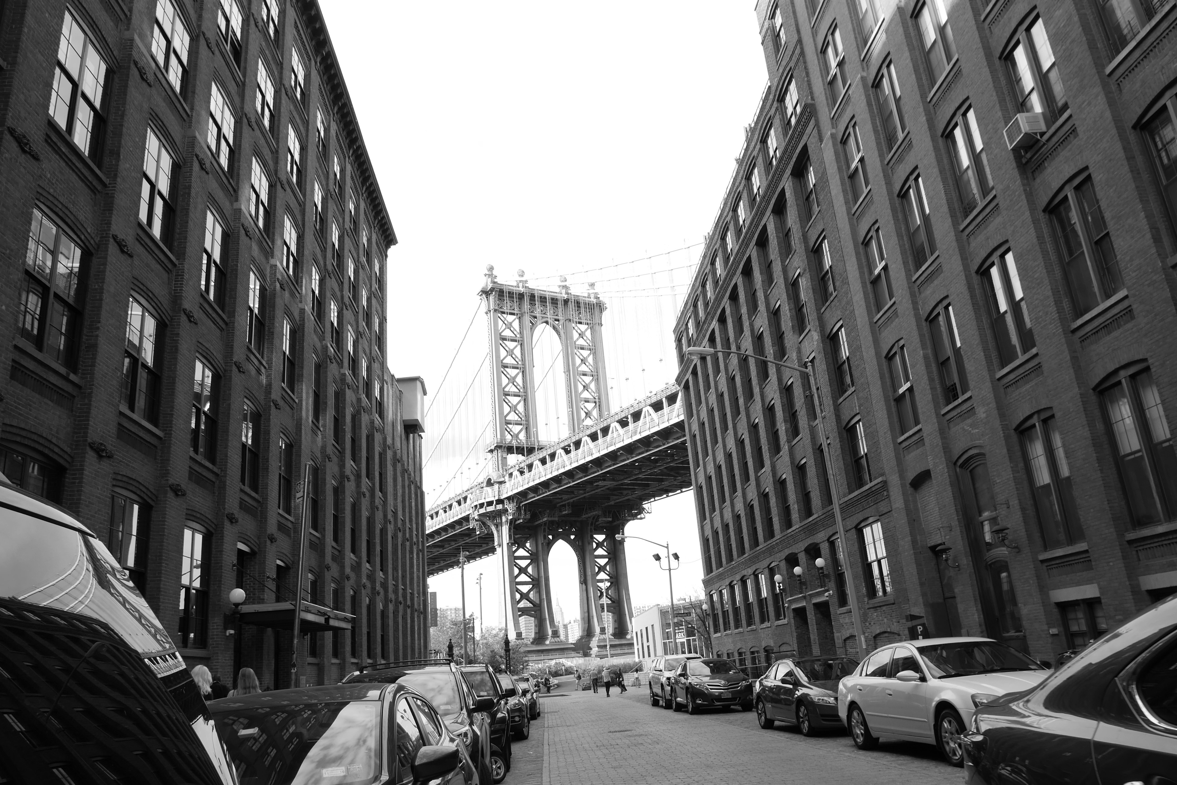 Street view featuring Manhattan Bridge surrounded by buildings and parked cars