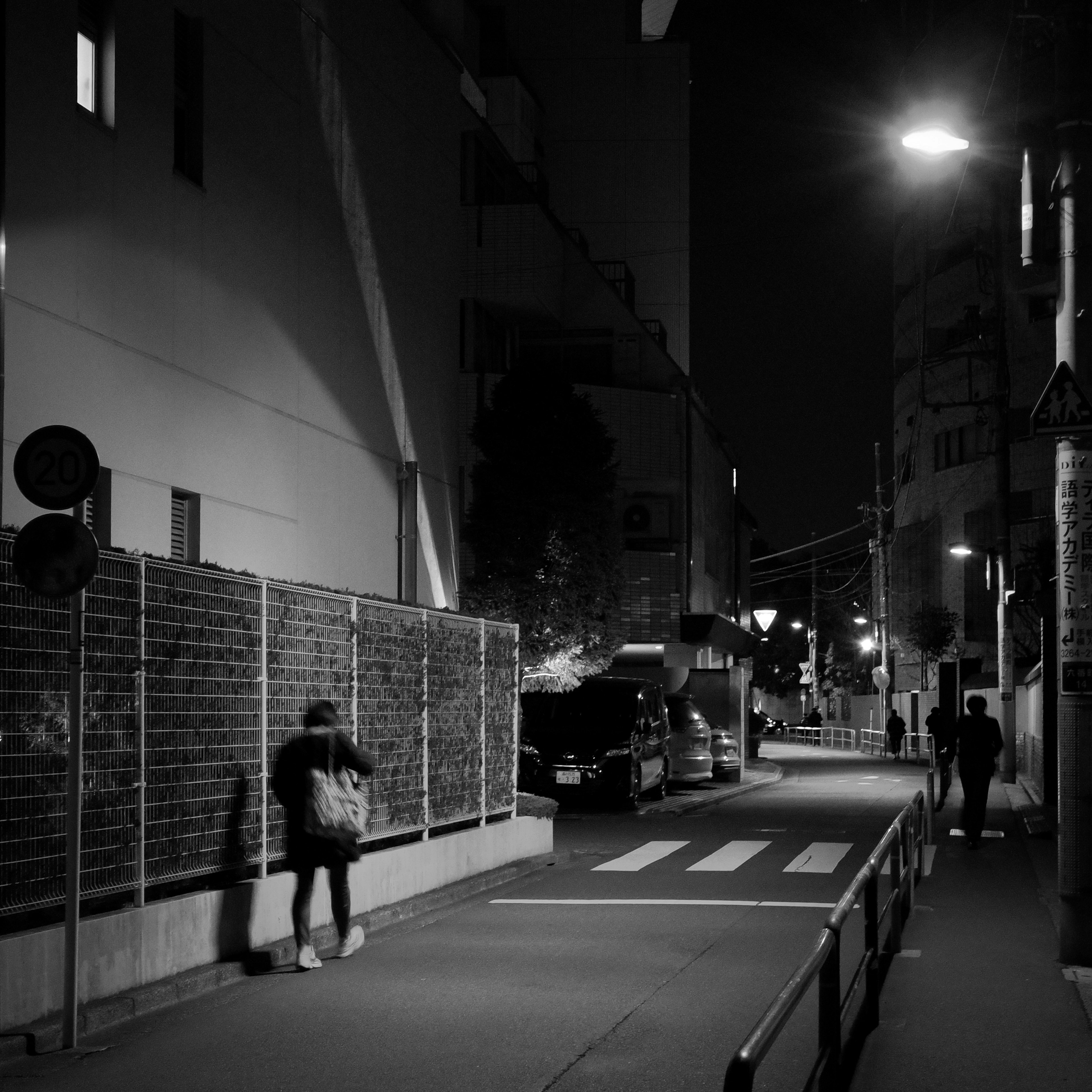 Una figura caminando en una calle nocturna con farolas y sombras