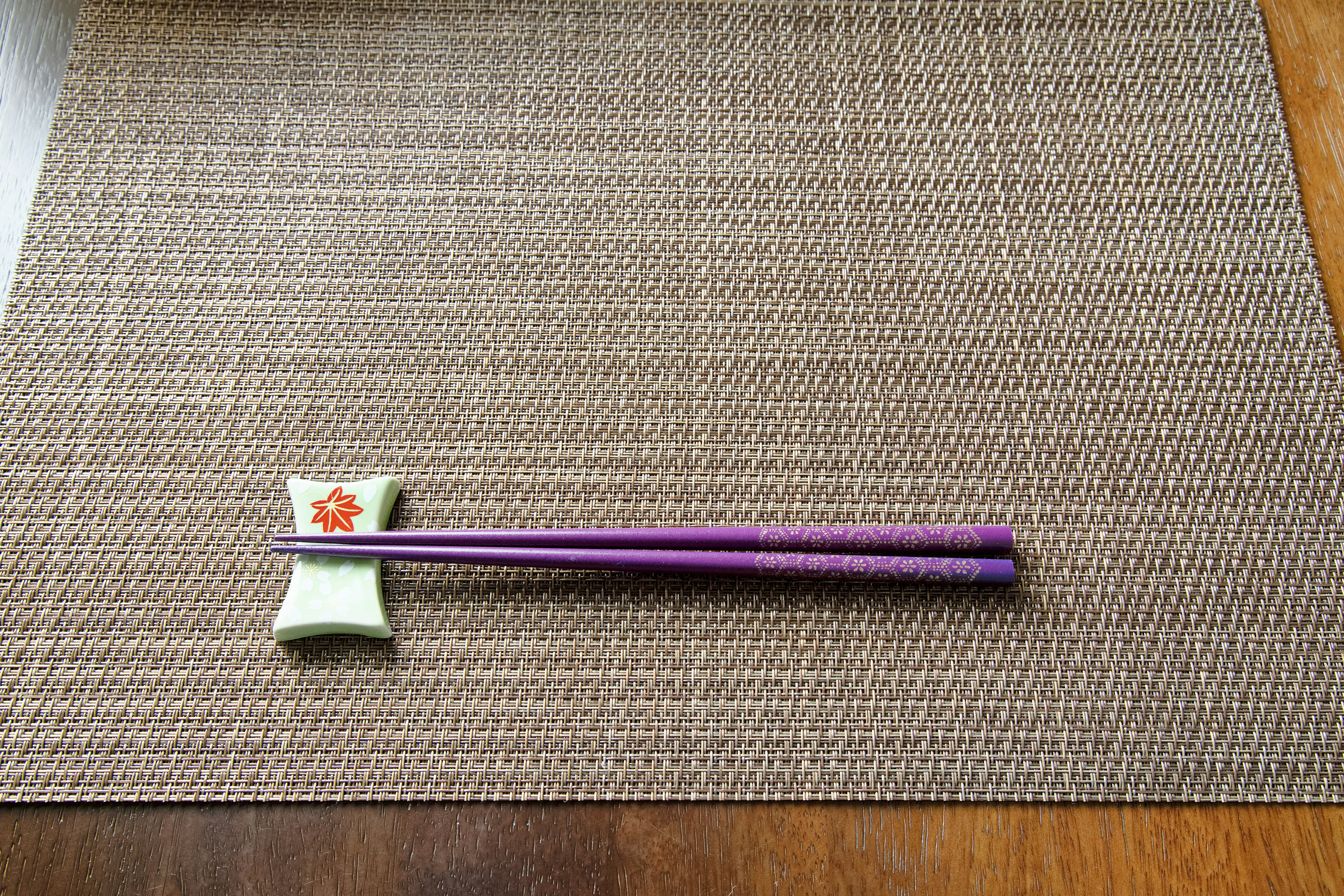 Purple chopsticks resting on a decorative chopstick holder on a table mat