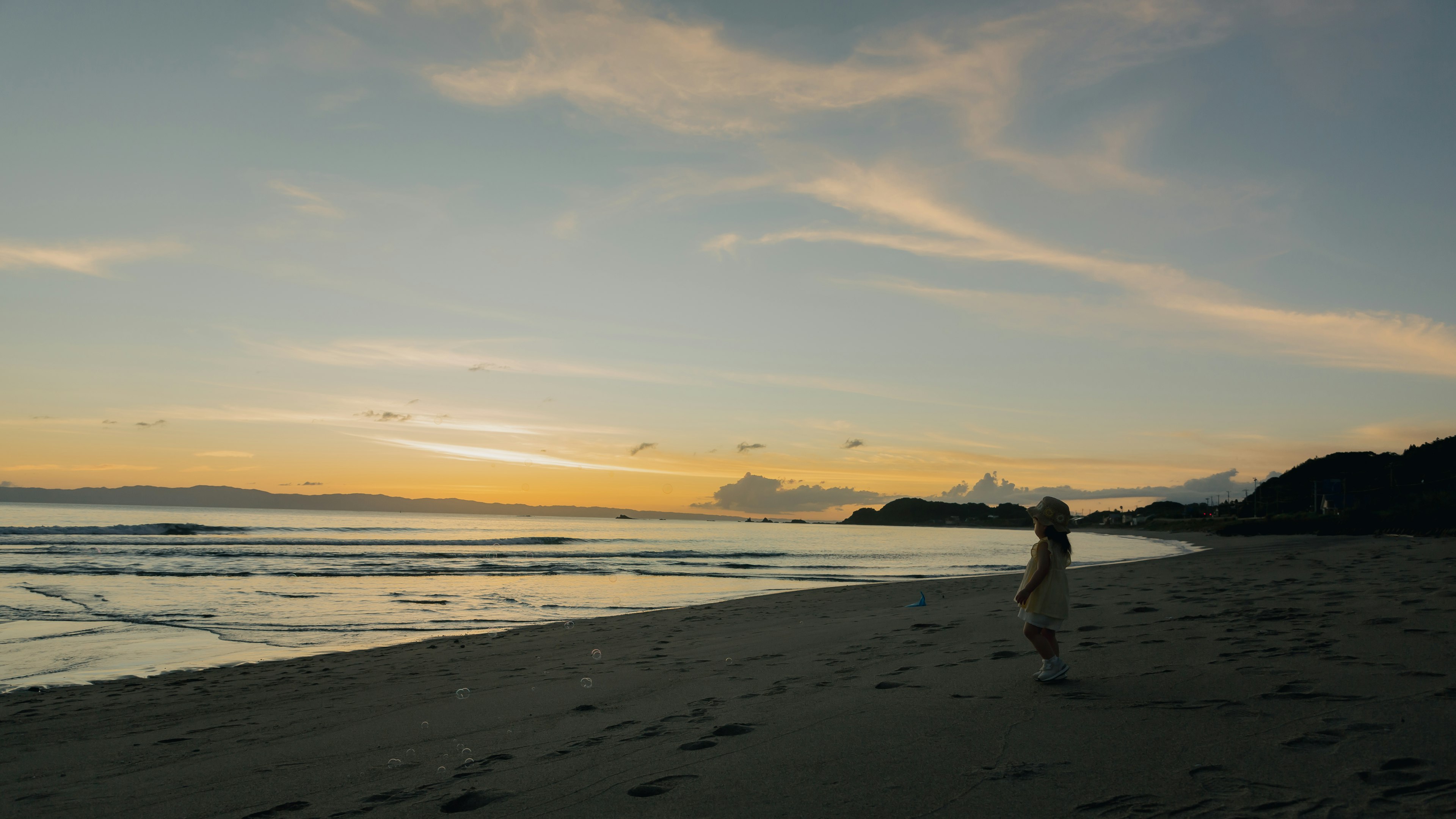 Orang berjalan di pantai saat matahari terbenam dengan awan dan ombak