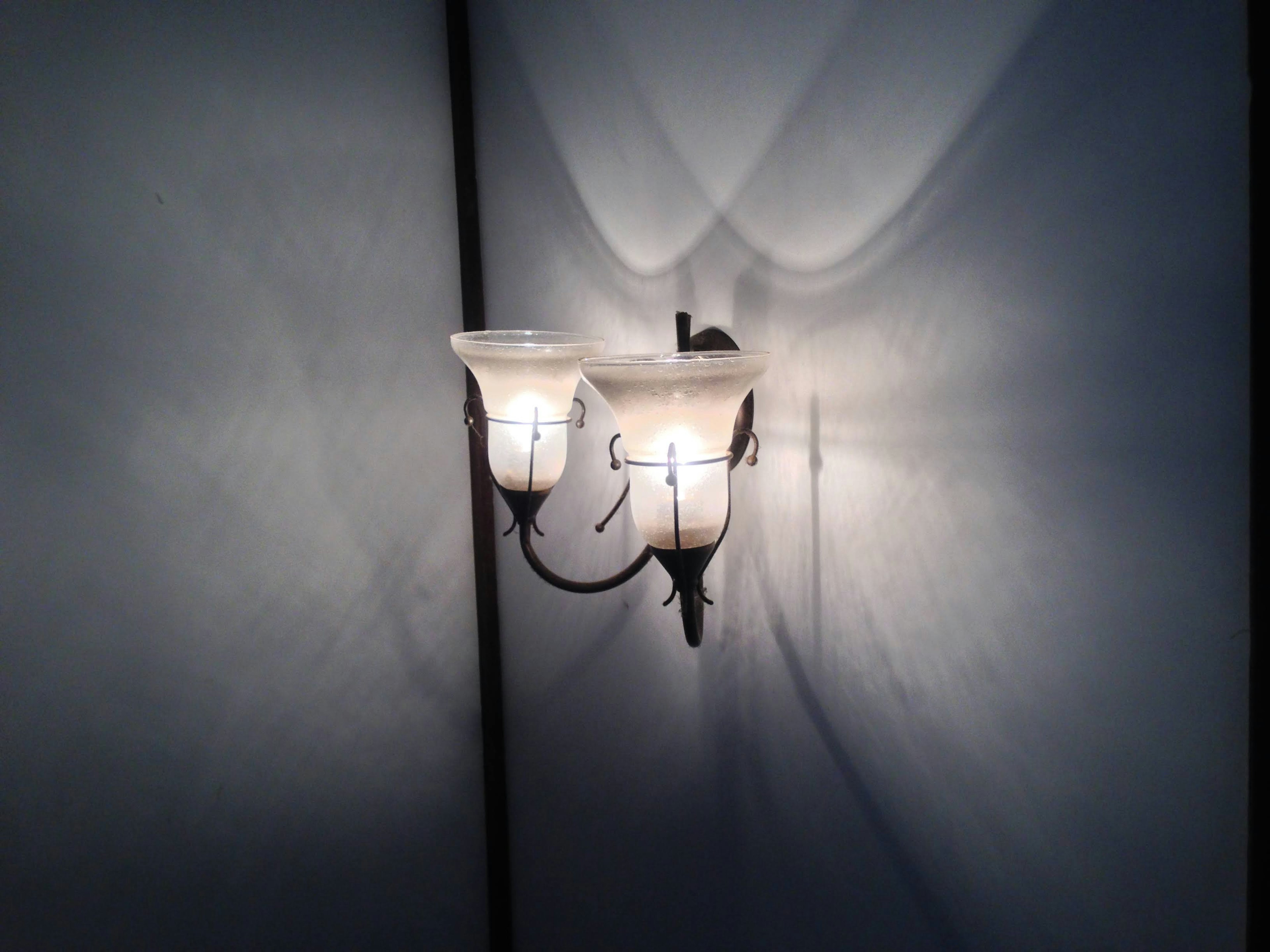 Two-light wall sconce emitting soft light and casting shadows on the wall