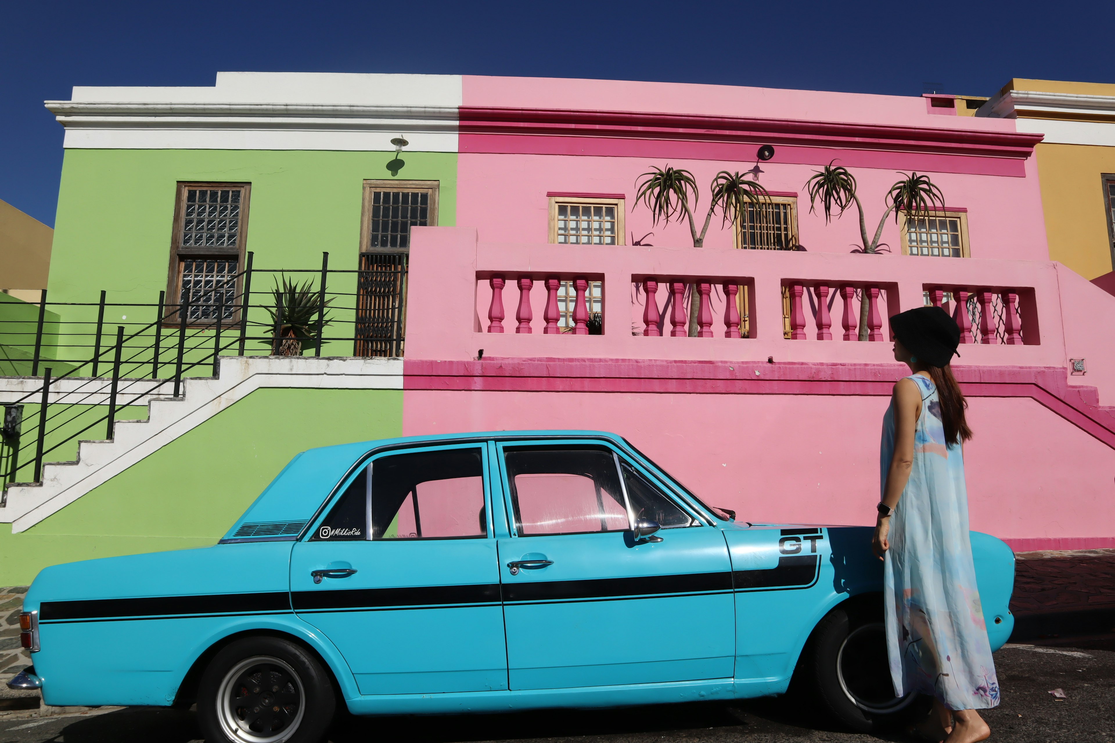 Woman standing next to a blue car in front of colorful buildings