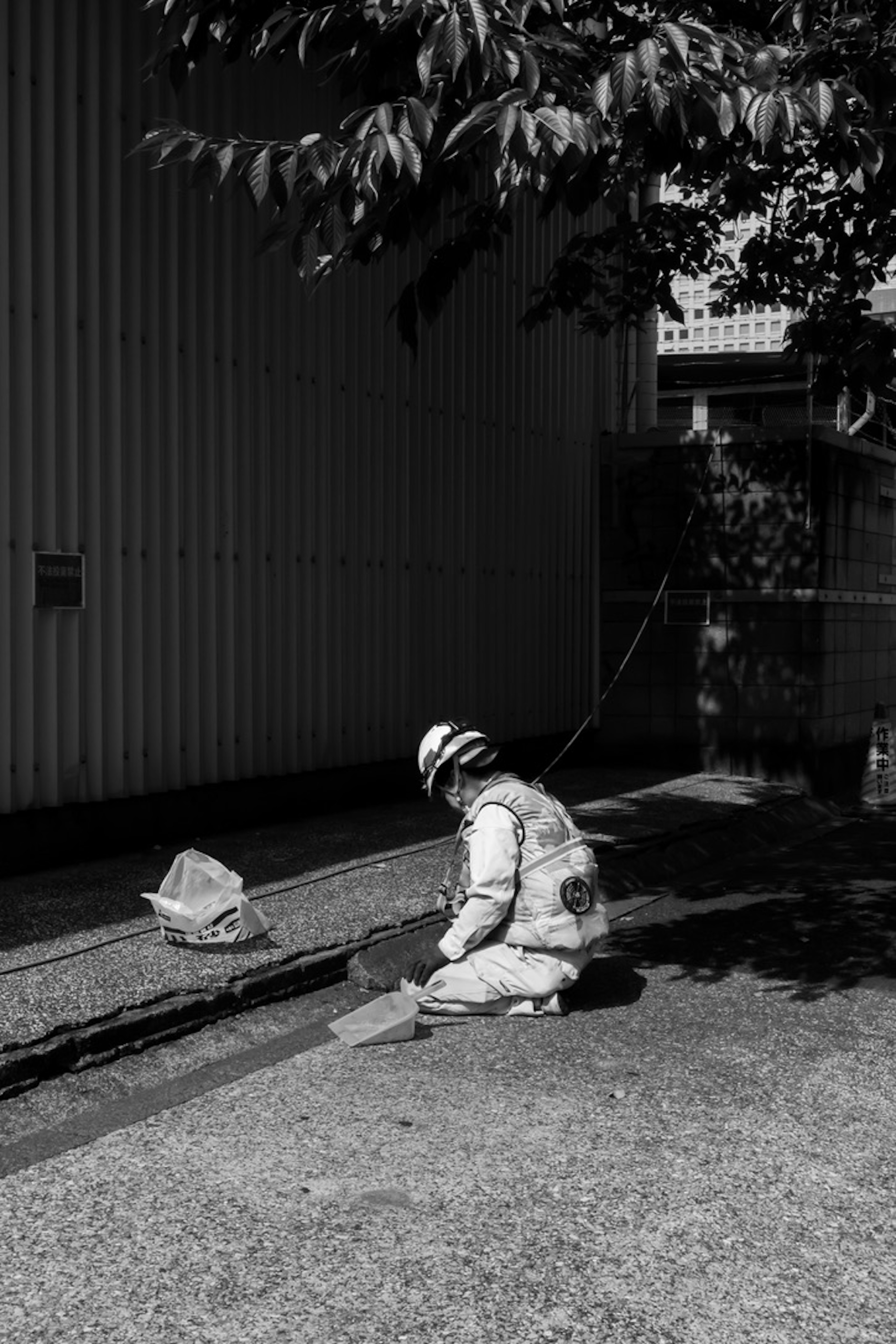 Un trabajador con ropa de seguridad sentado en el suelo y trabajando en una imagen en blanco y negro