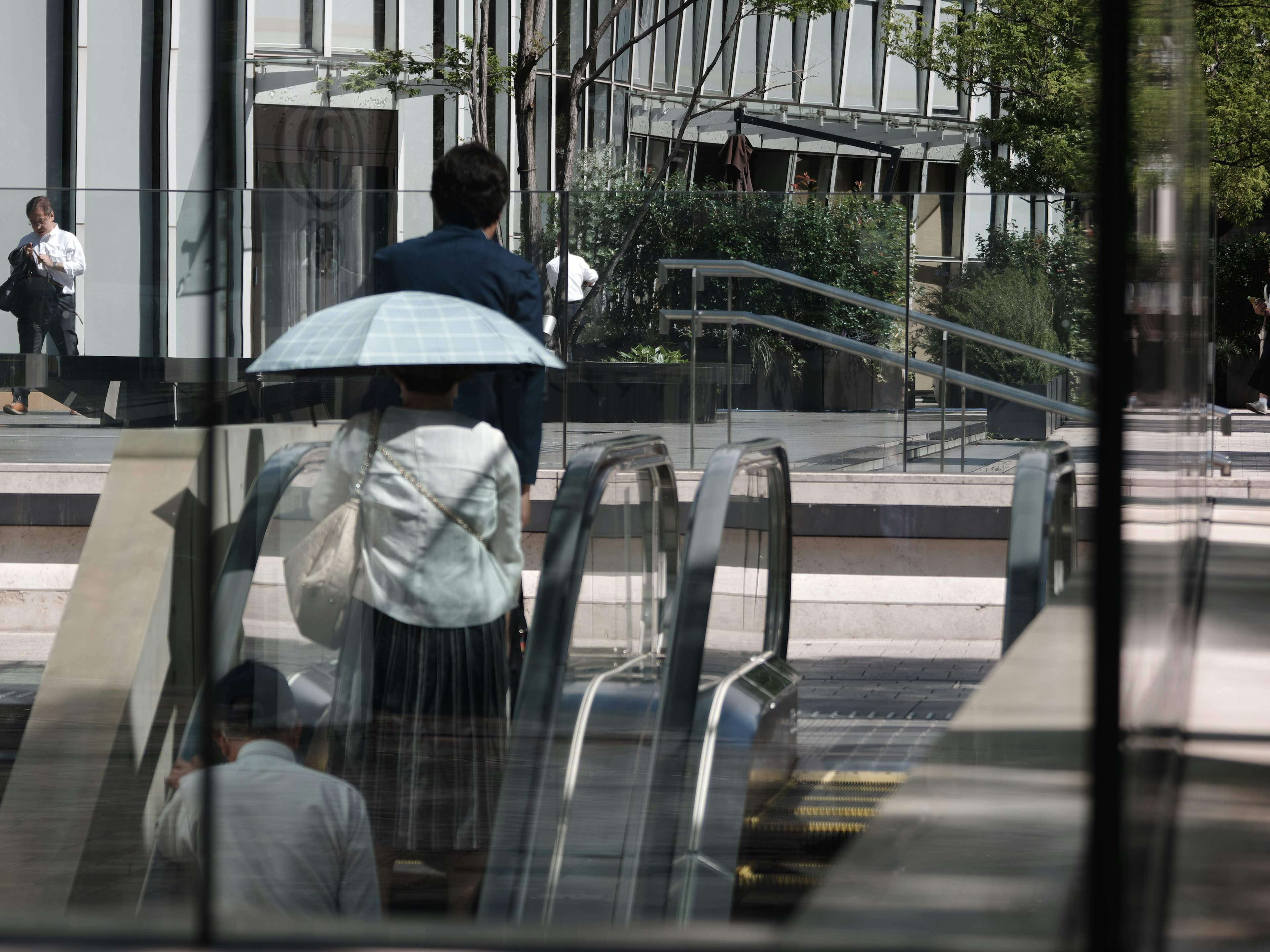 Eine Frau mit einem Regenschirm und ein Mann mit dem Rücken zur Kamera in der Nähe einer Rolltreppe