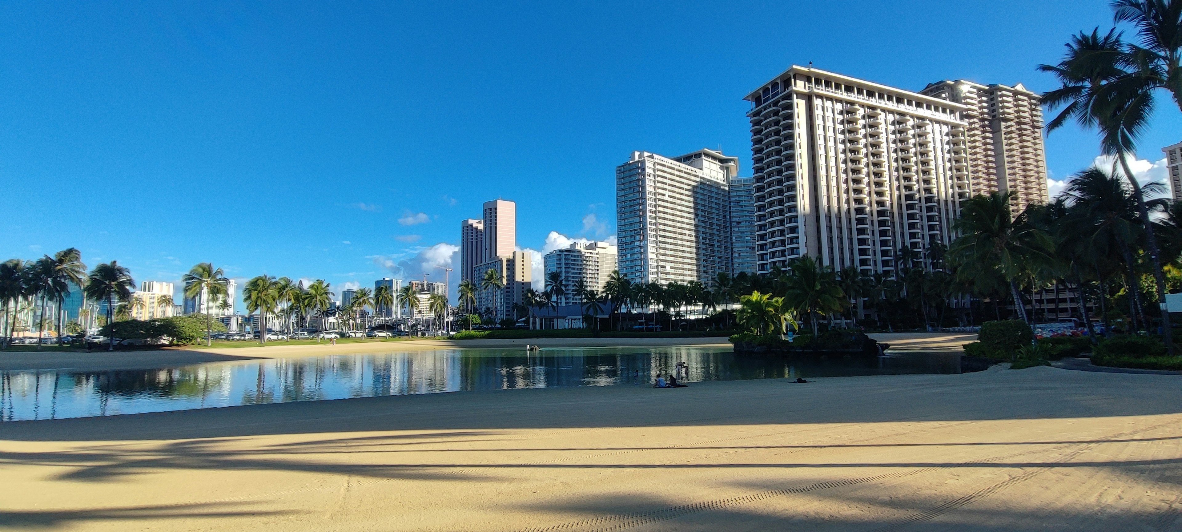 ทิวทัศน์ชายหาดกับท้องฟ้าสีฟ้าและตึกระฟ้าที่สะท้อนในน้ำ