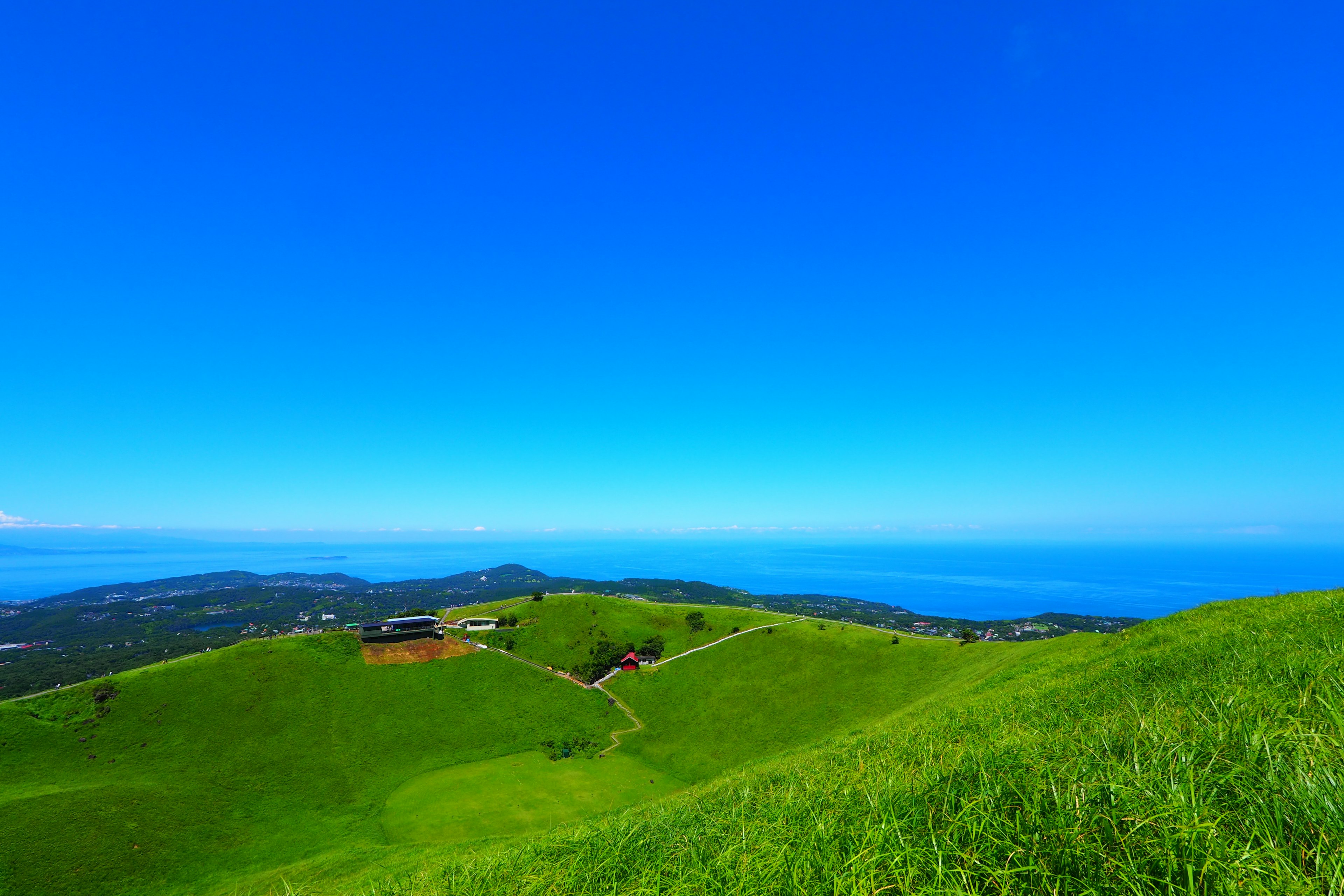 Vista escénica de colinas verdes bajo un cielo azul con un océano distante