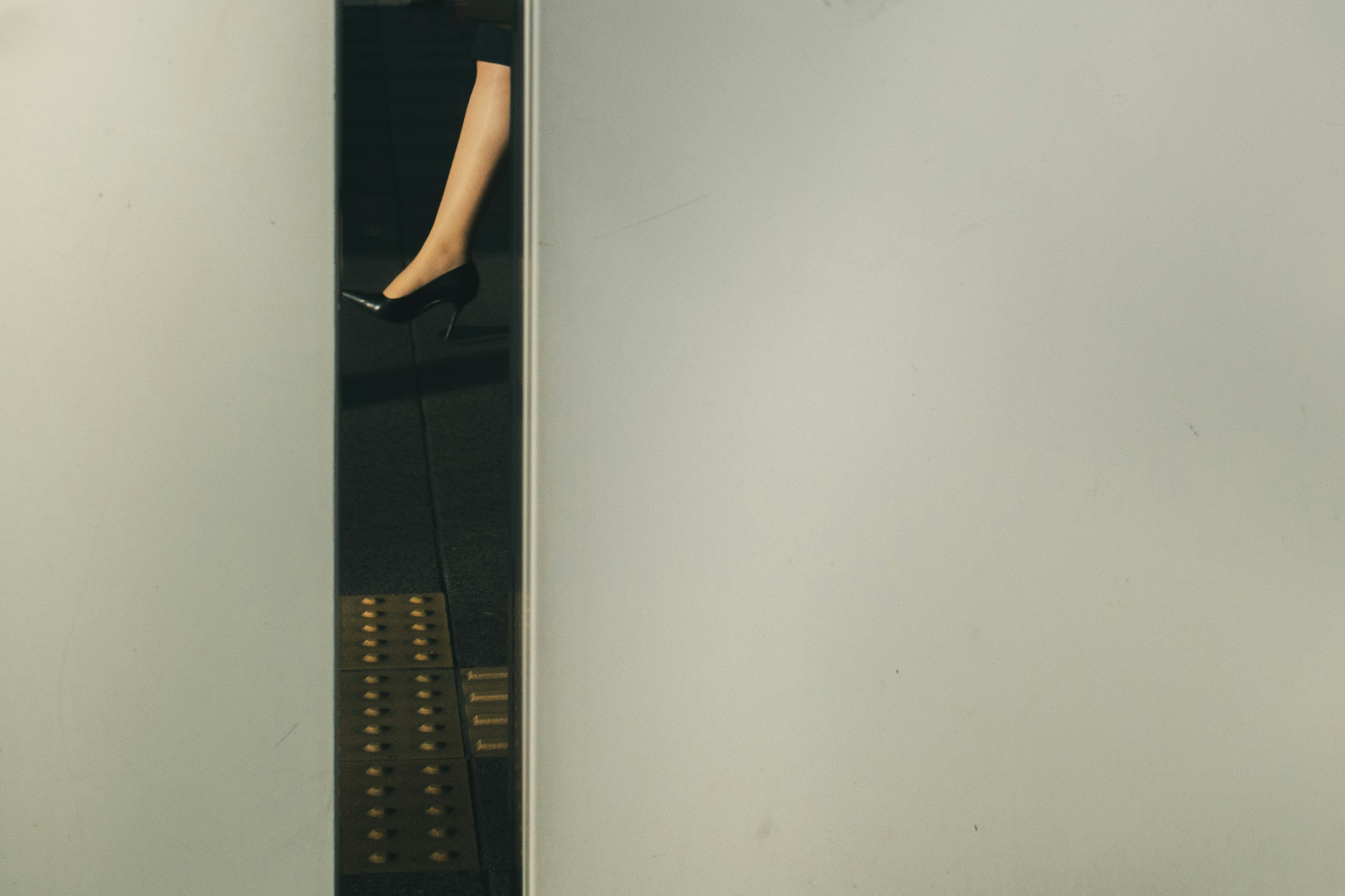 A woman's leg and high heel visible through a gap in an elevator door