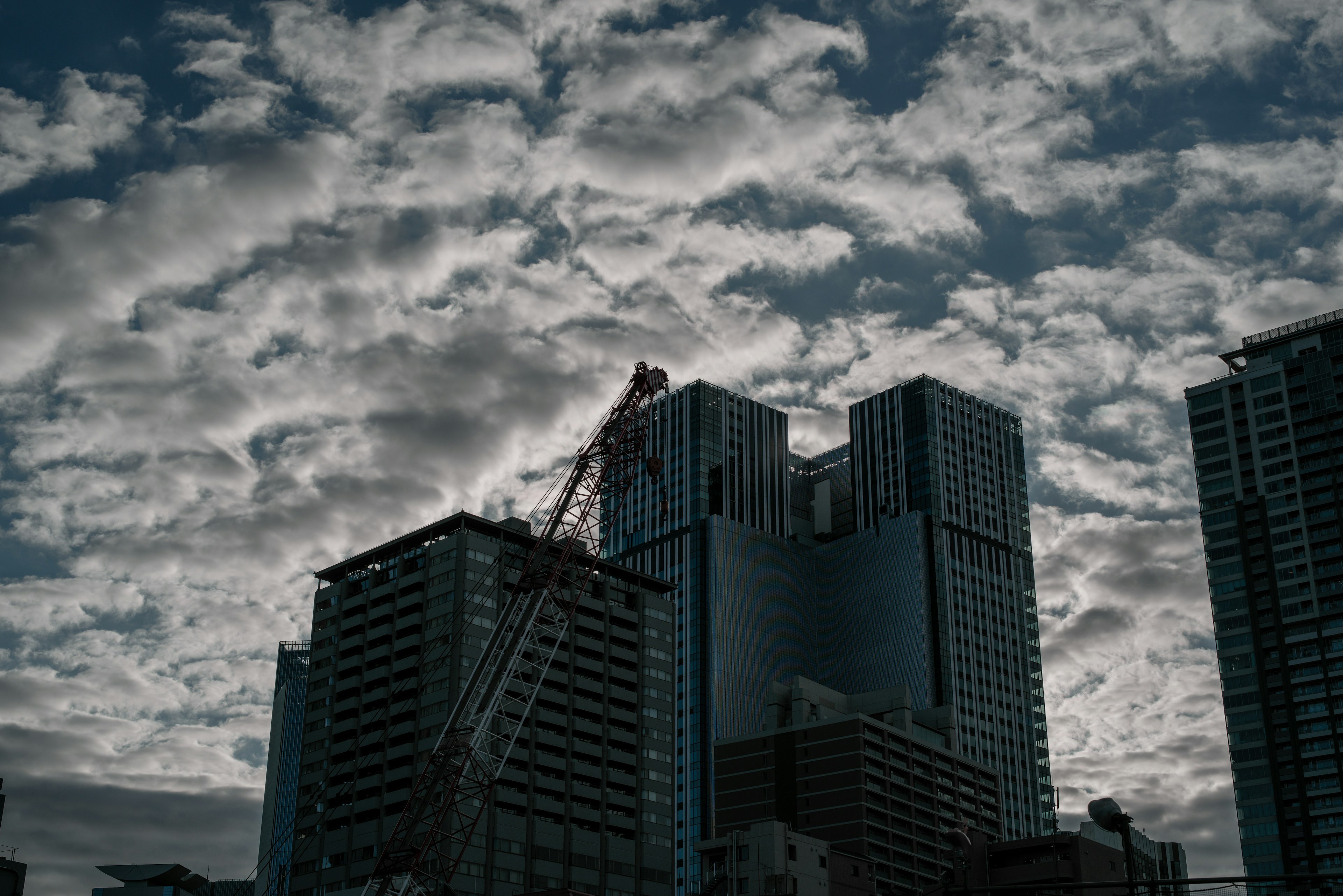 暗い雲に覆われた高層ビルとクレーンのシルエット