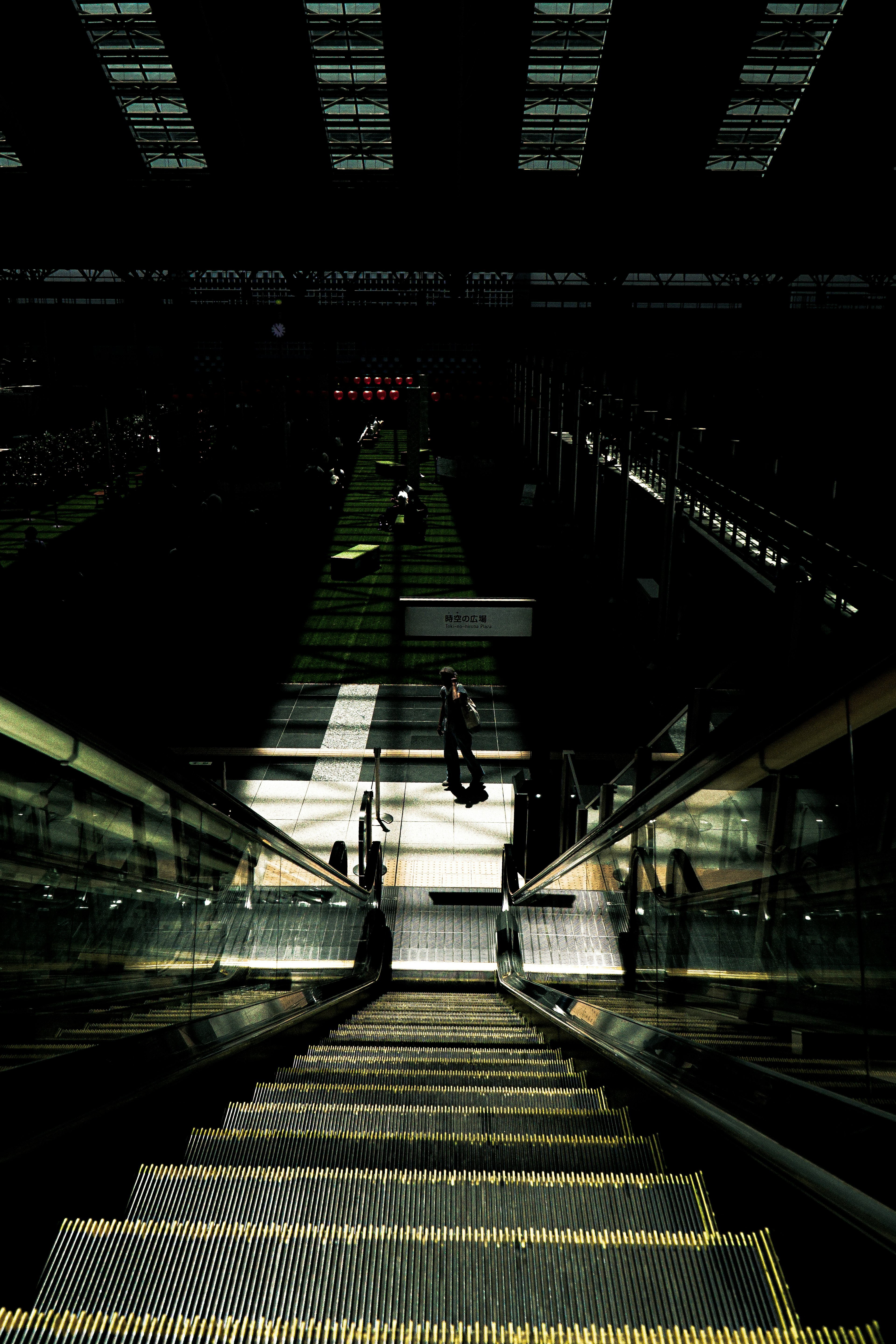 View down an escalator into a dimly lit space with scattered lighting